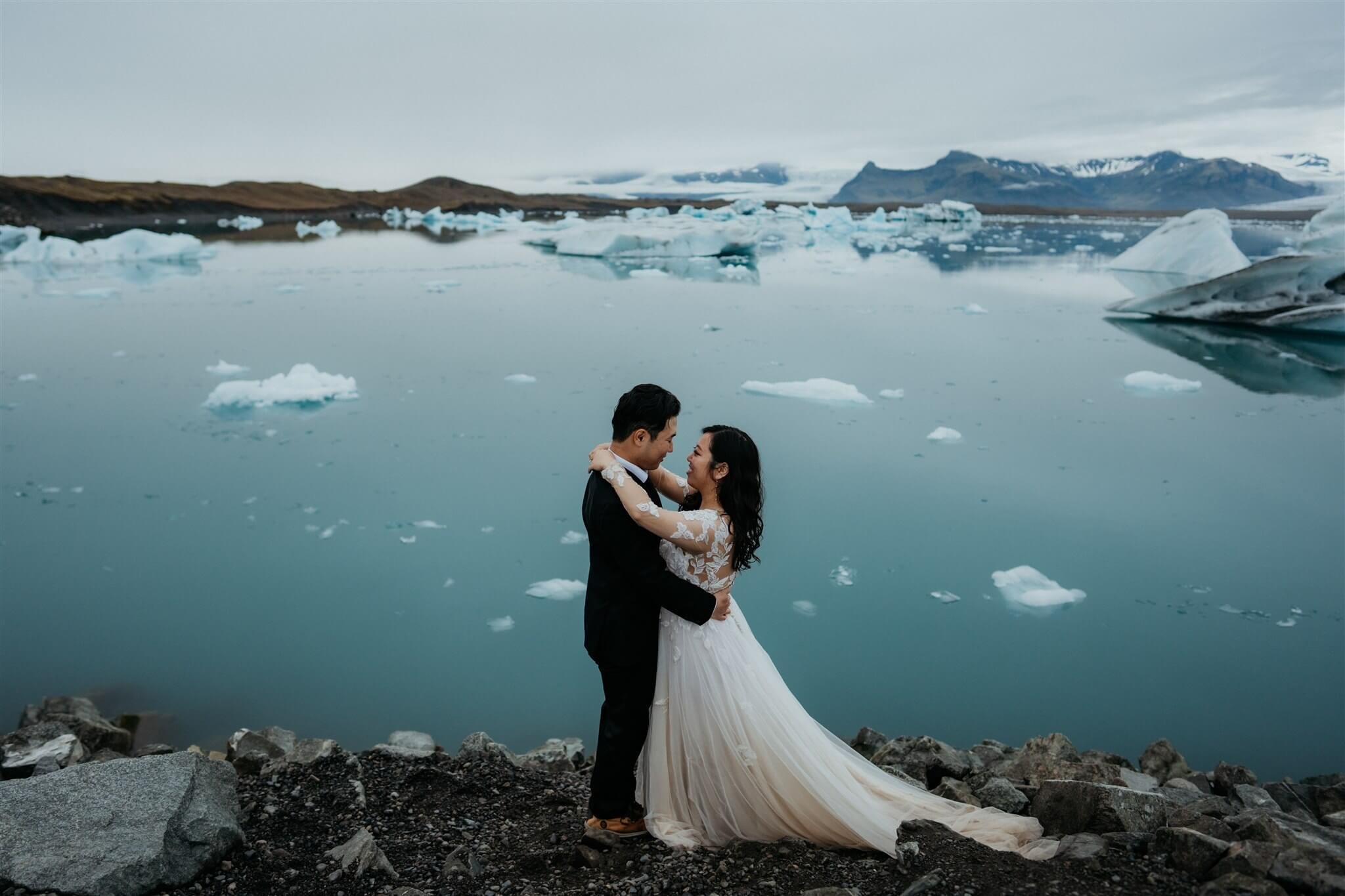 Bride and groom dance on a black sand beach by an icy lagoon while eloping in Iceland