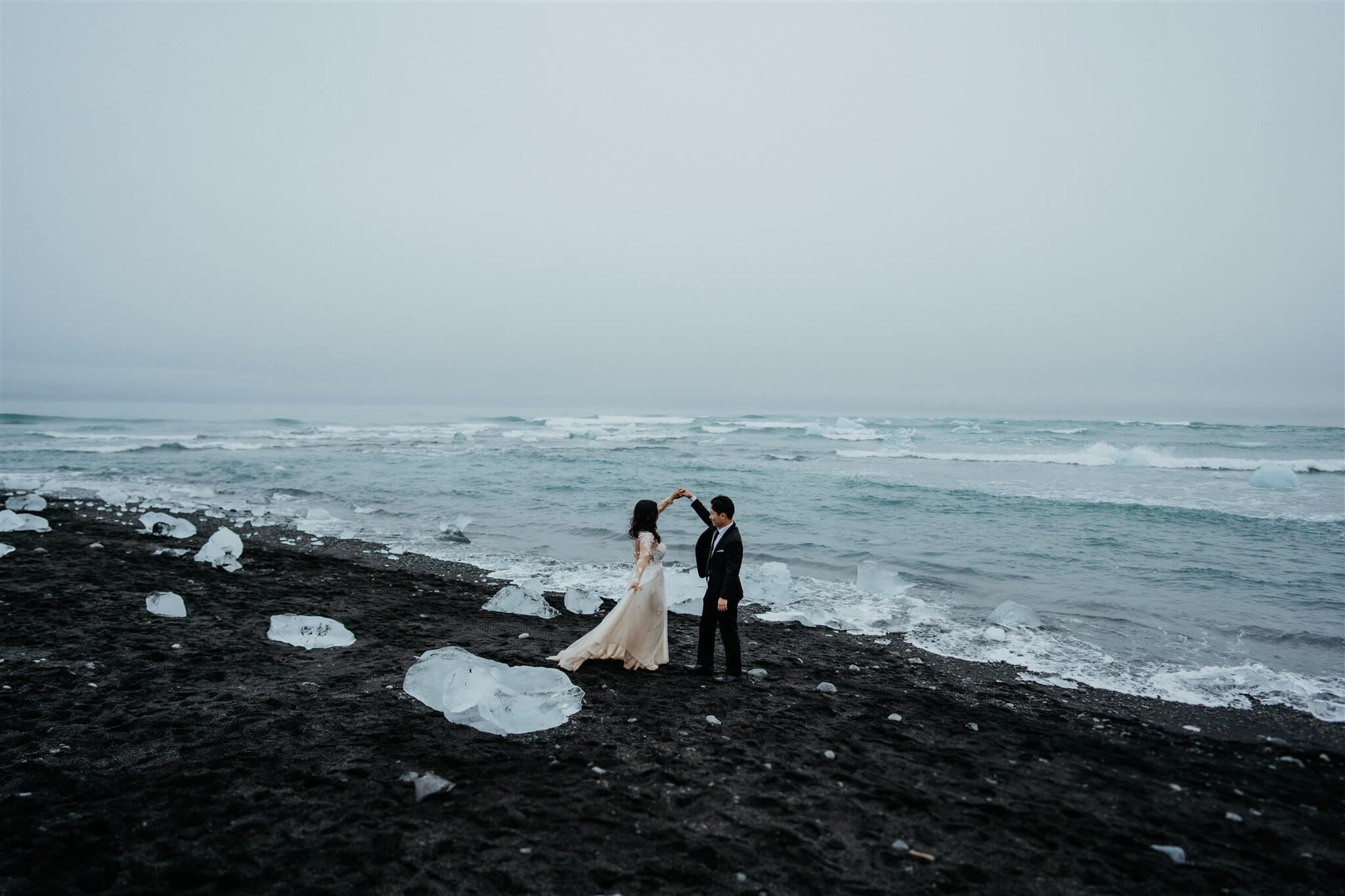 Bride and groom dance on a black sand beach by an icy lagoon after they elope in Iceland