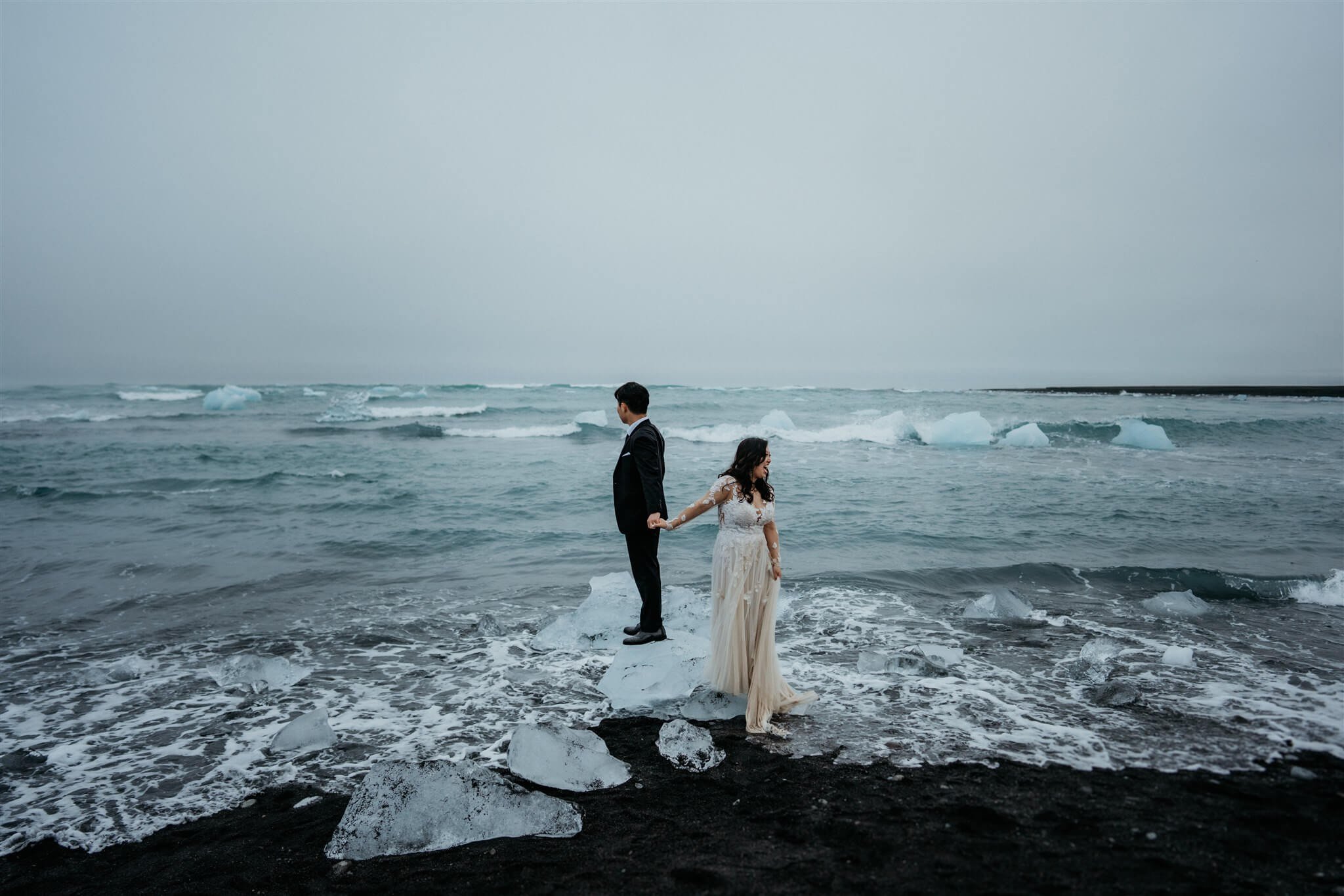 Bride and groom standing on ice on a black sand beach in Iceland