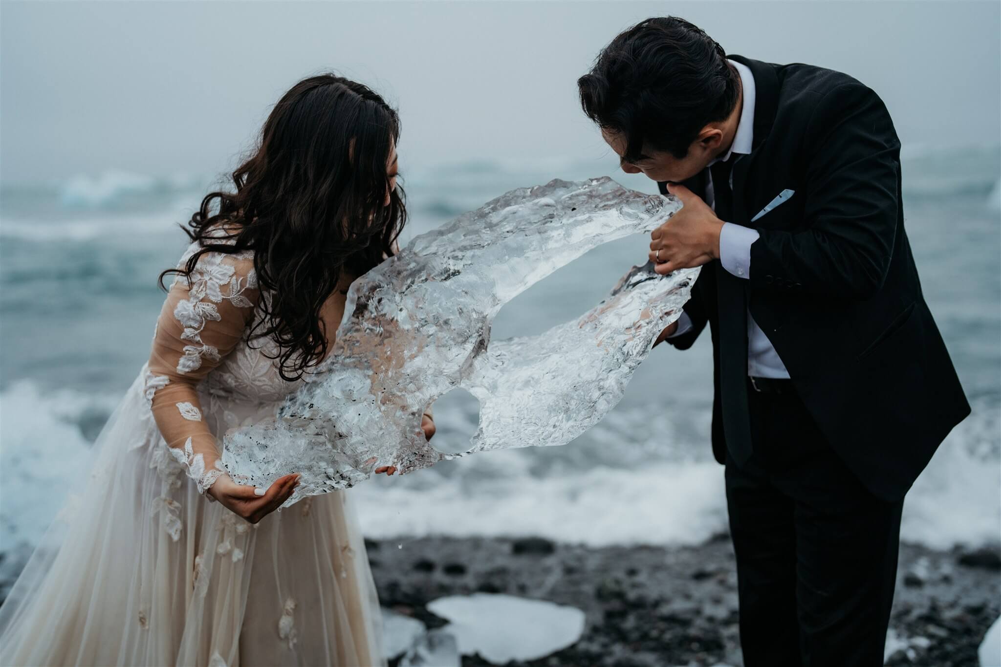 Bride and groom lick a piece of ice off the black sand beach in Iceland
