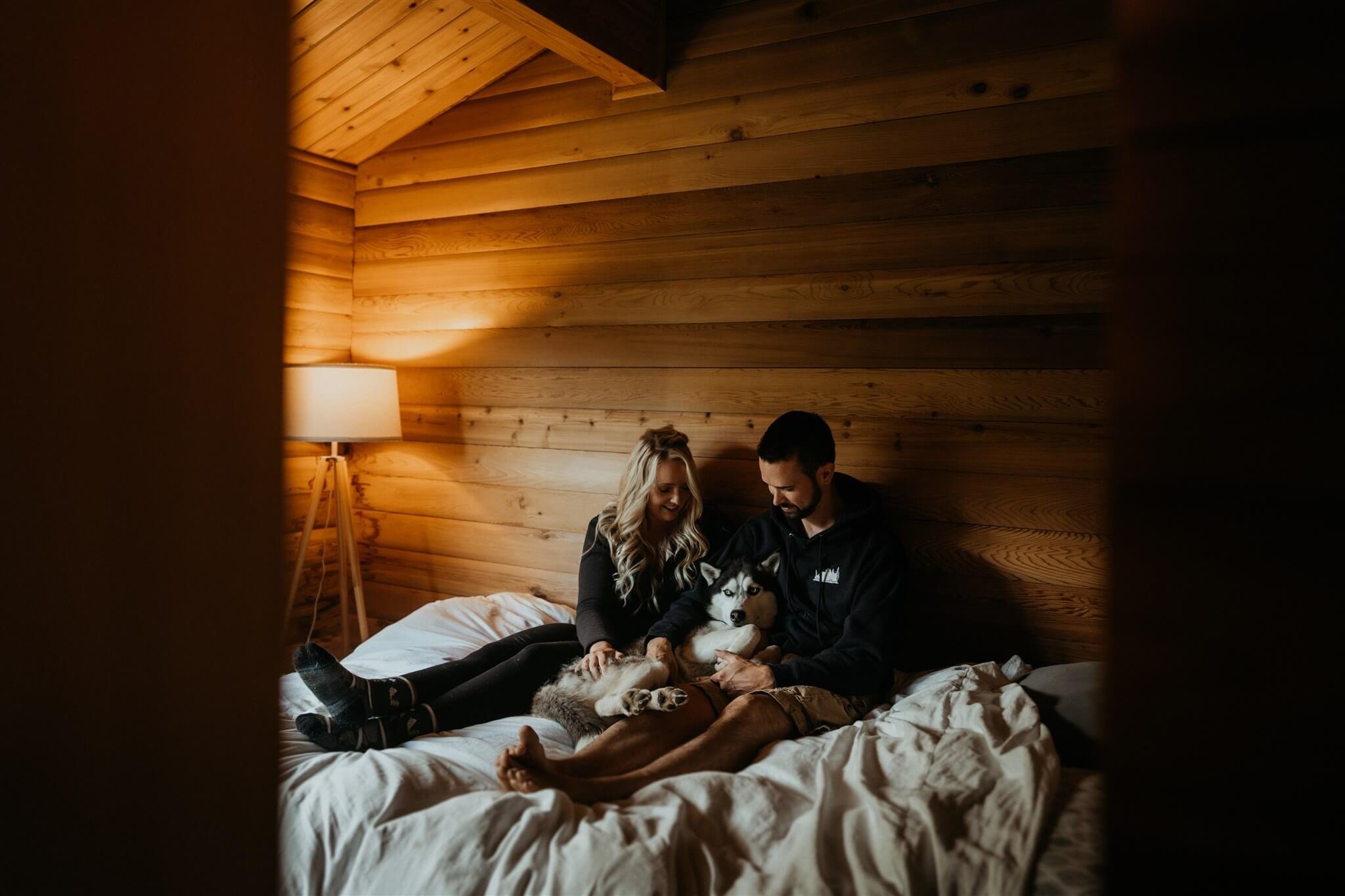 Bride and groom cuddling with their black and white husky on the bed