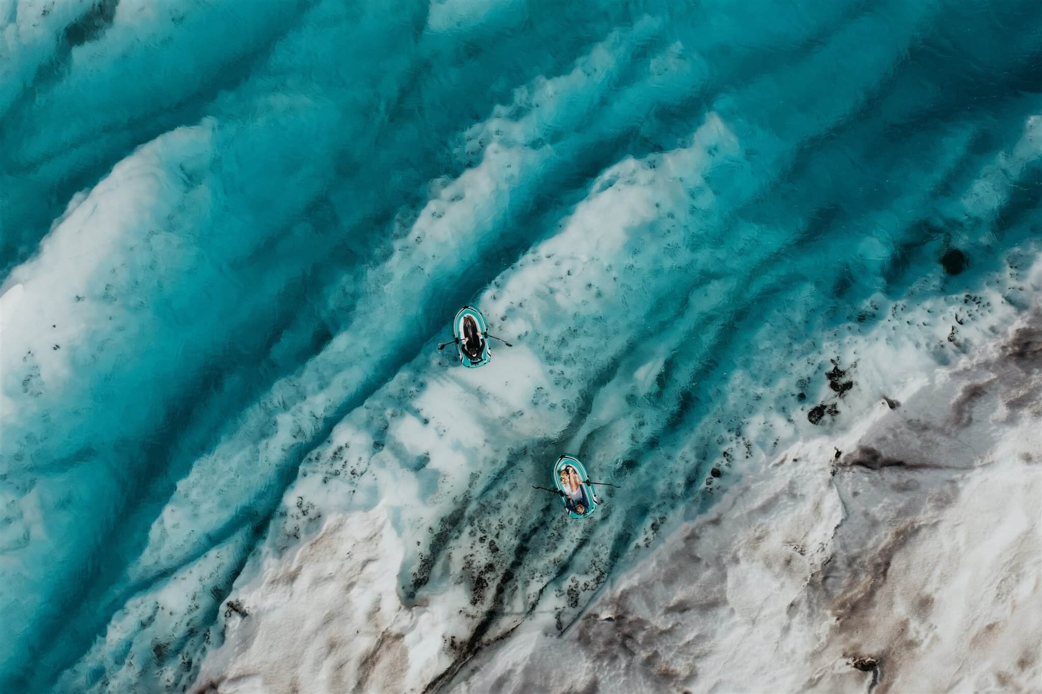 Bride and groom paddle inflatable boats on a glacier pond in Alaska