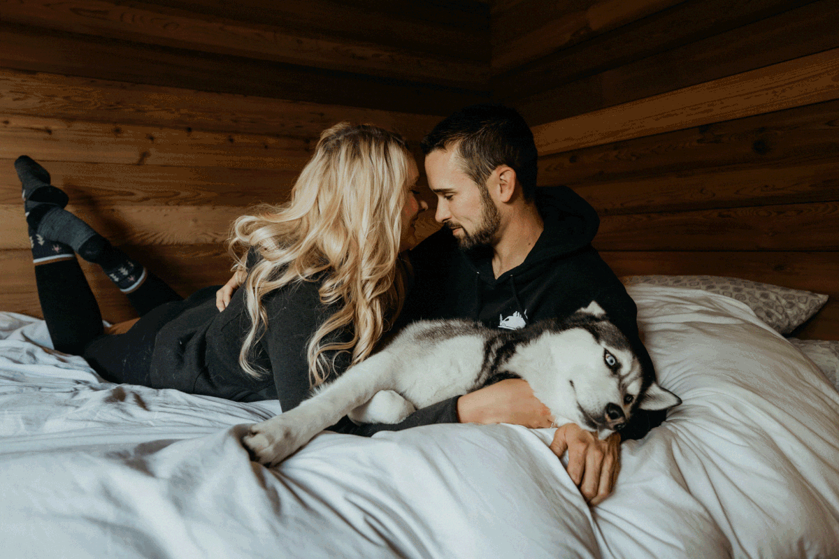 Bride and groom cuddling with their black and white husky on the bed
