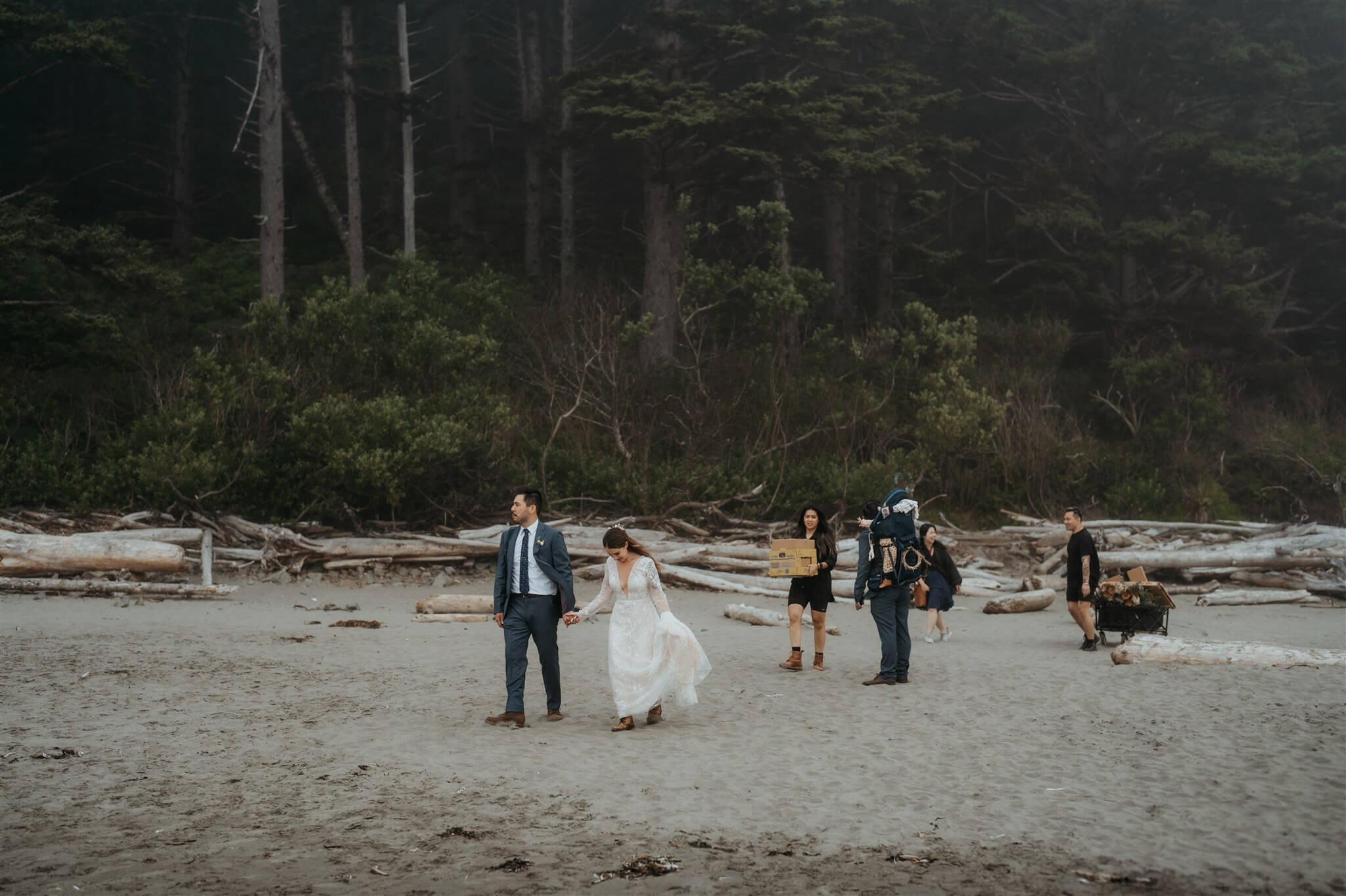 Bride and groom holding hands and walking across the beach for their elopement with family