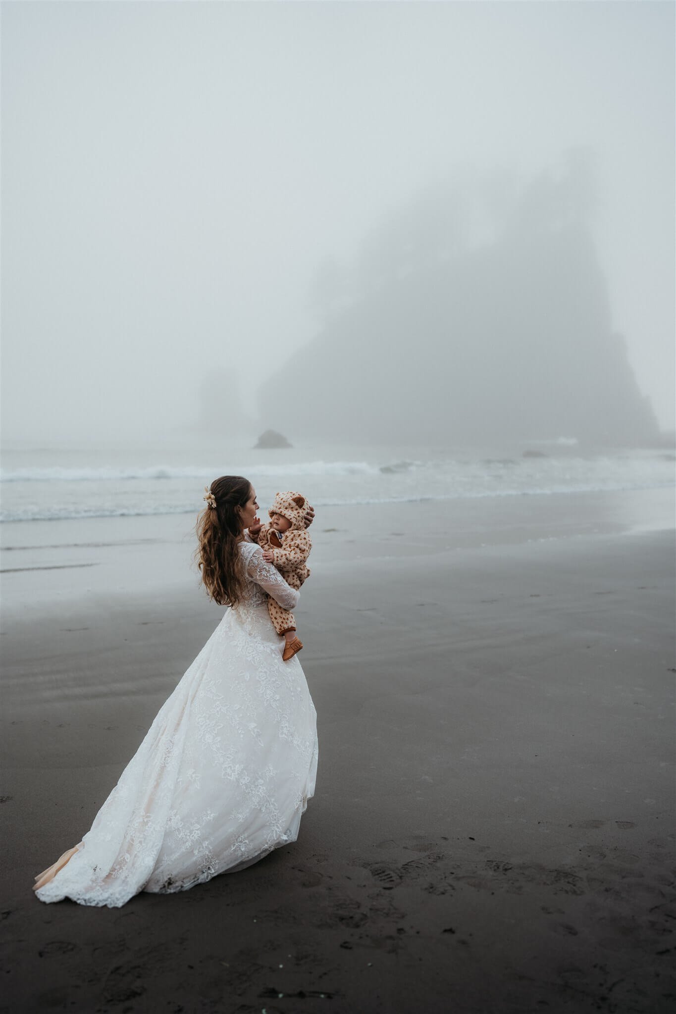 Bride holding baby while walking across La Push Beach 