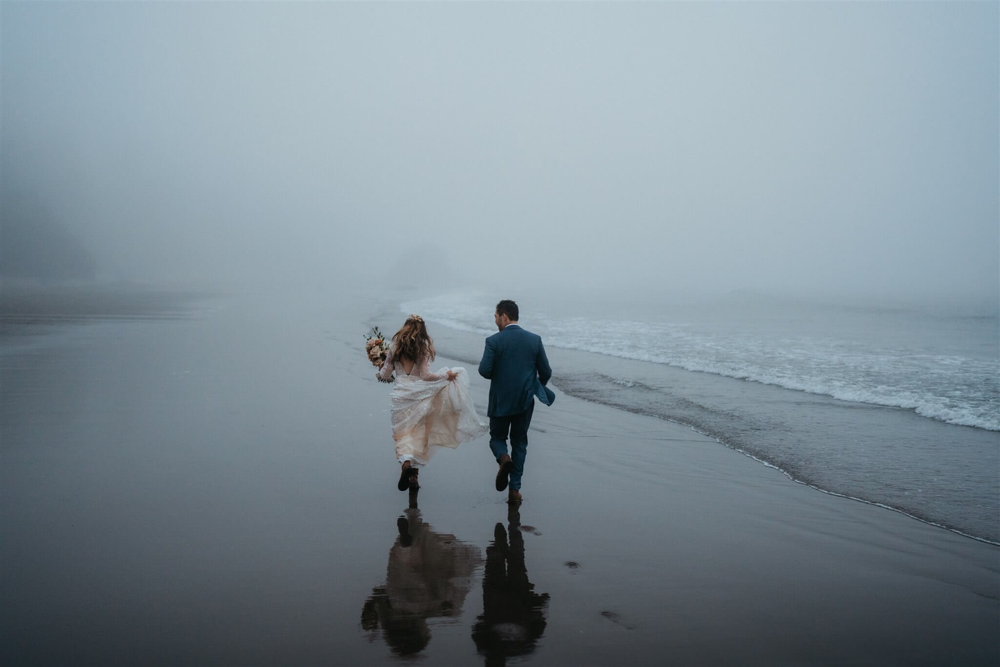 Bride and groom running across the beach after eloping with family