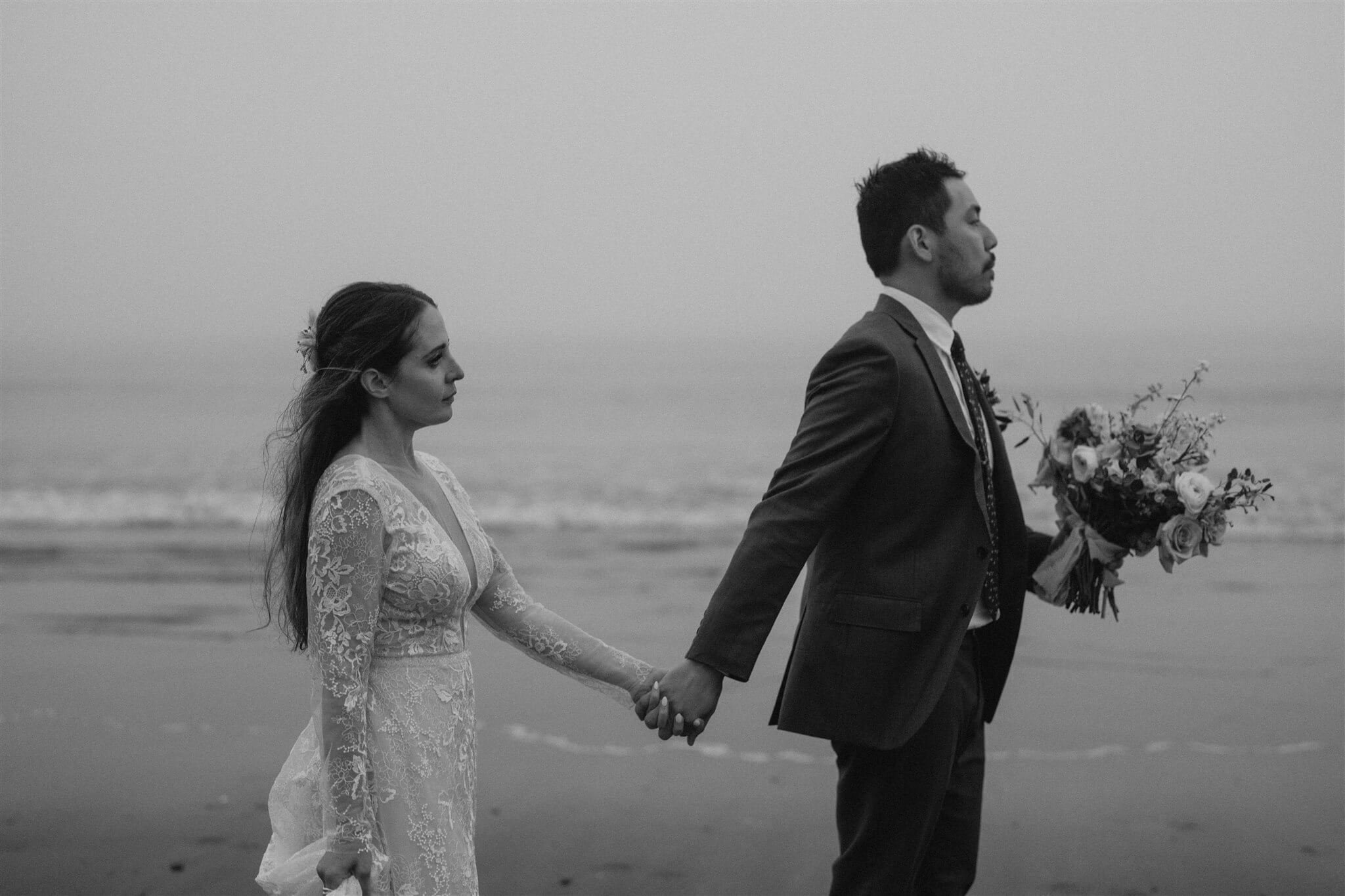 Bride and groom holding hands while walking across the beach in Olympic National Park