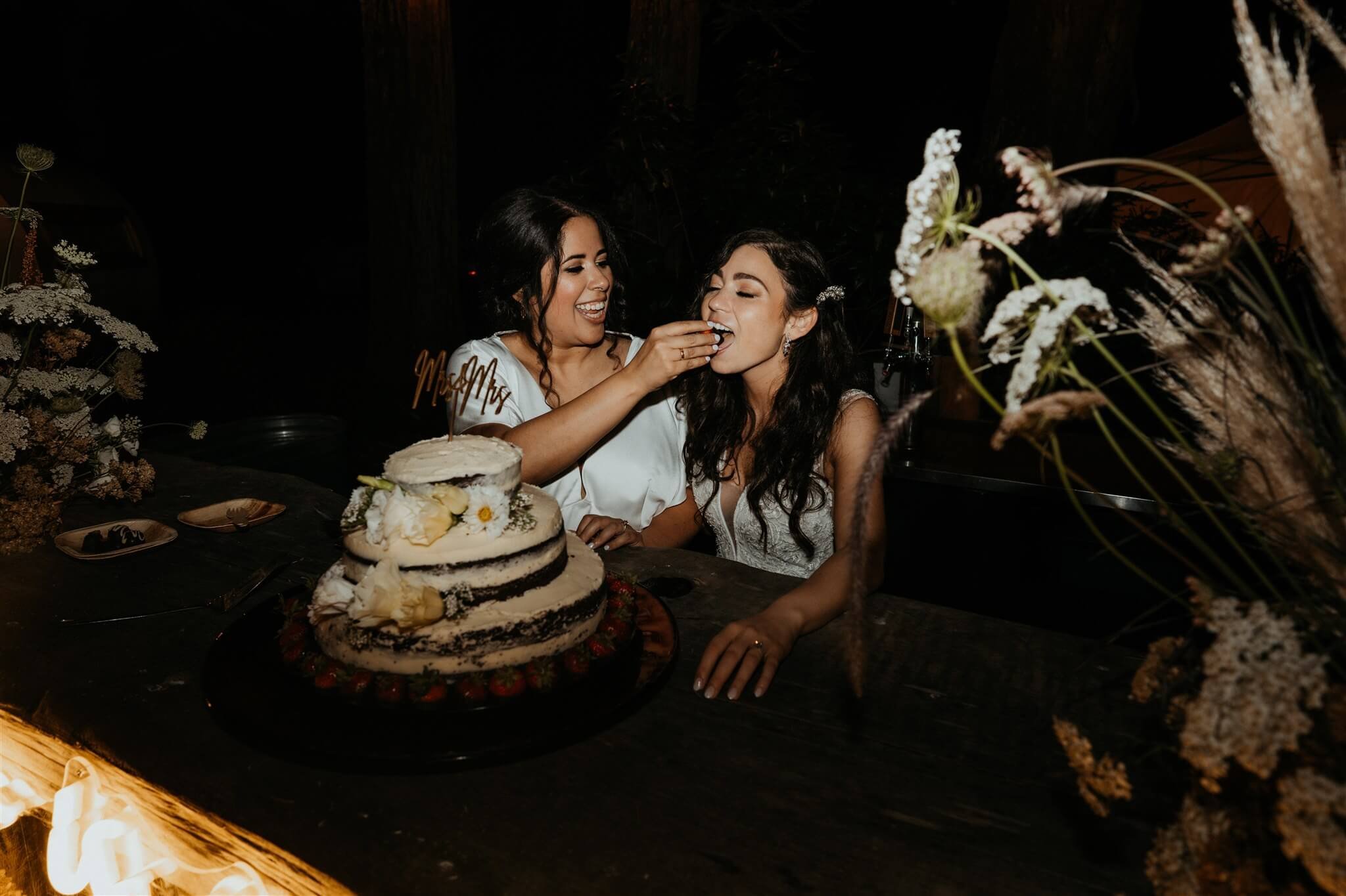 Brides feed each other cake at flower-filled wedding on the Oregon Coast
