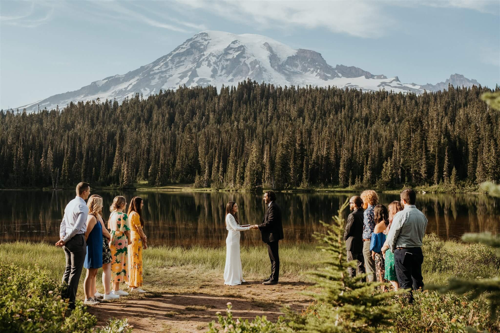 Bride and groom exchange vows by the lake in front of Mount Rainier at their intimate adventure wedding with friends