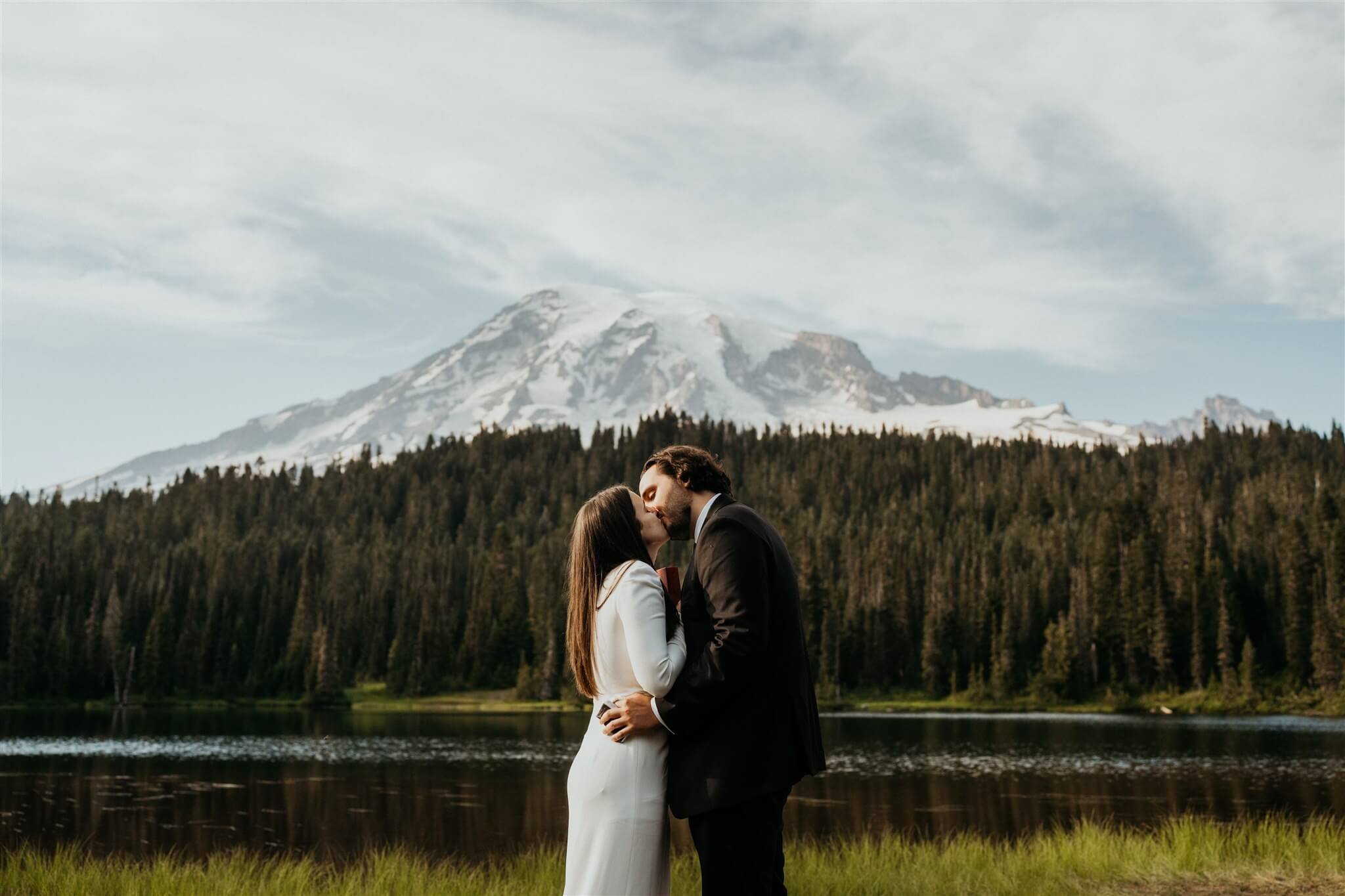 Bride and groom kiss in front of Mount Rainier at their adventure wedding with friends