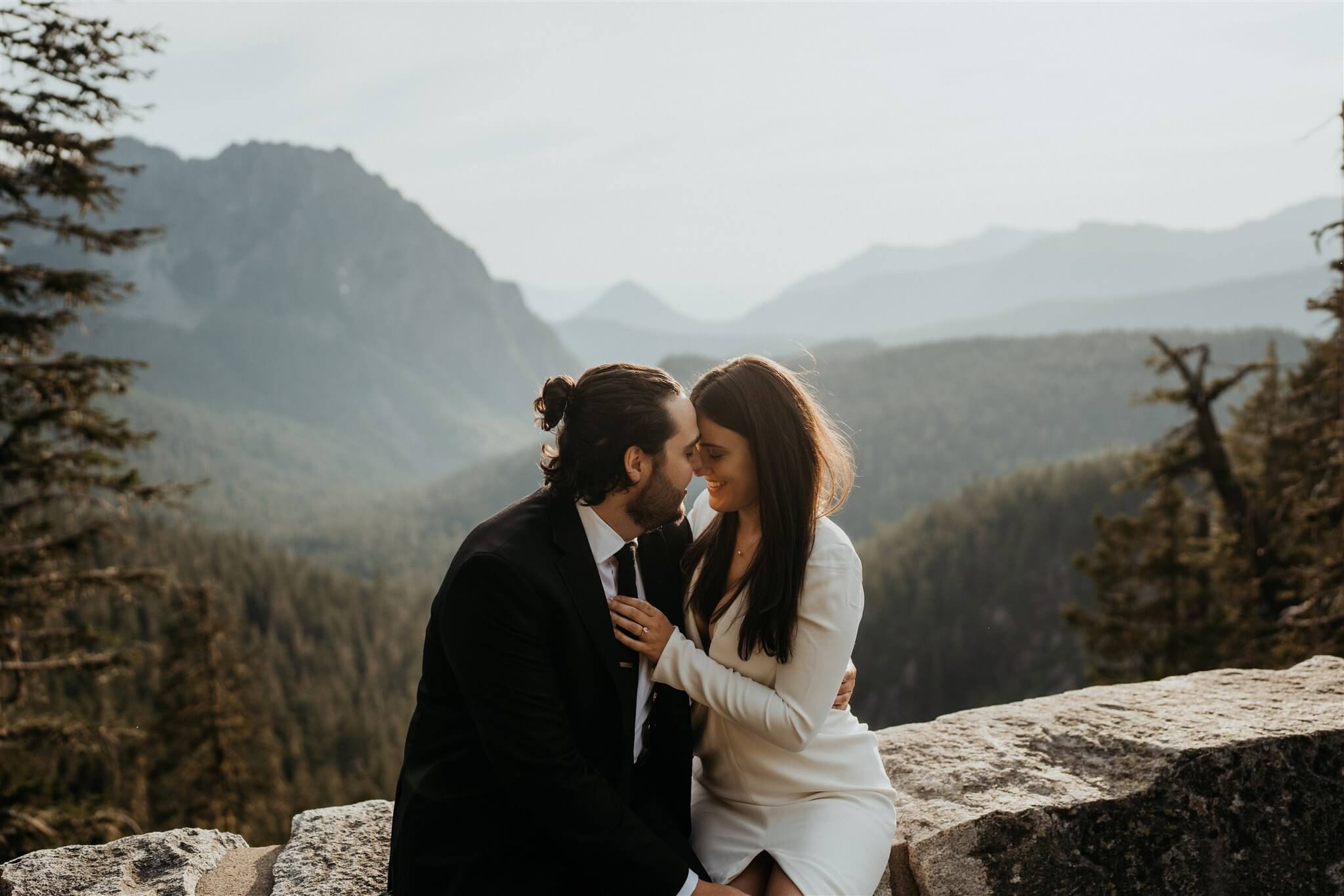 Bride and groom sit on a ledge during couple portraits at Mt Rainier