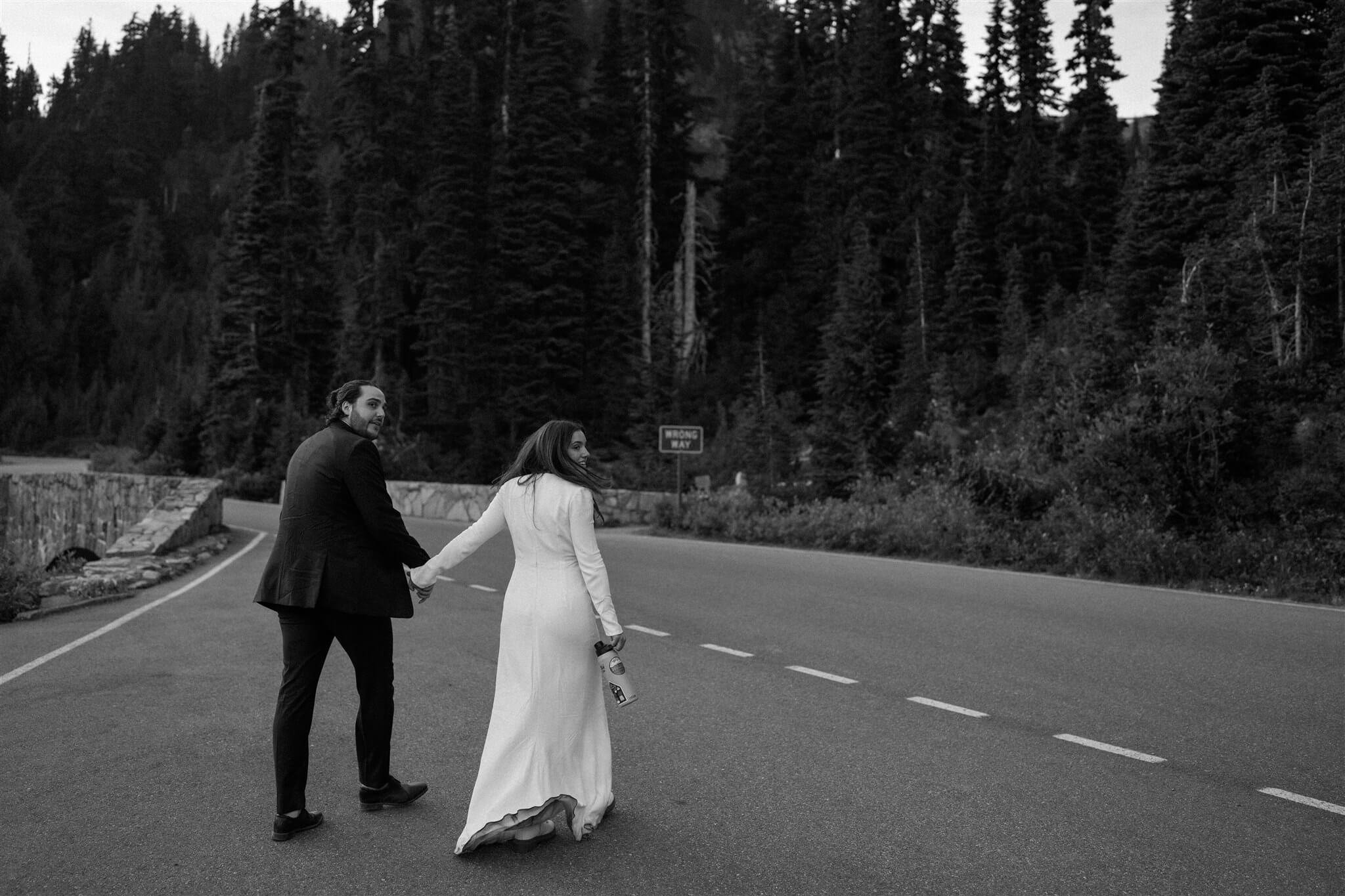 Bride and groom hold hands while running across the street at their adventure wedding at Mt Rainier