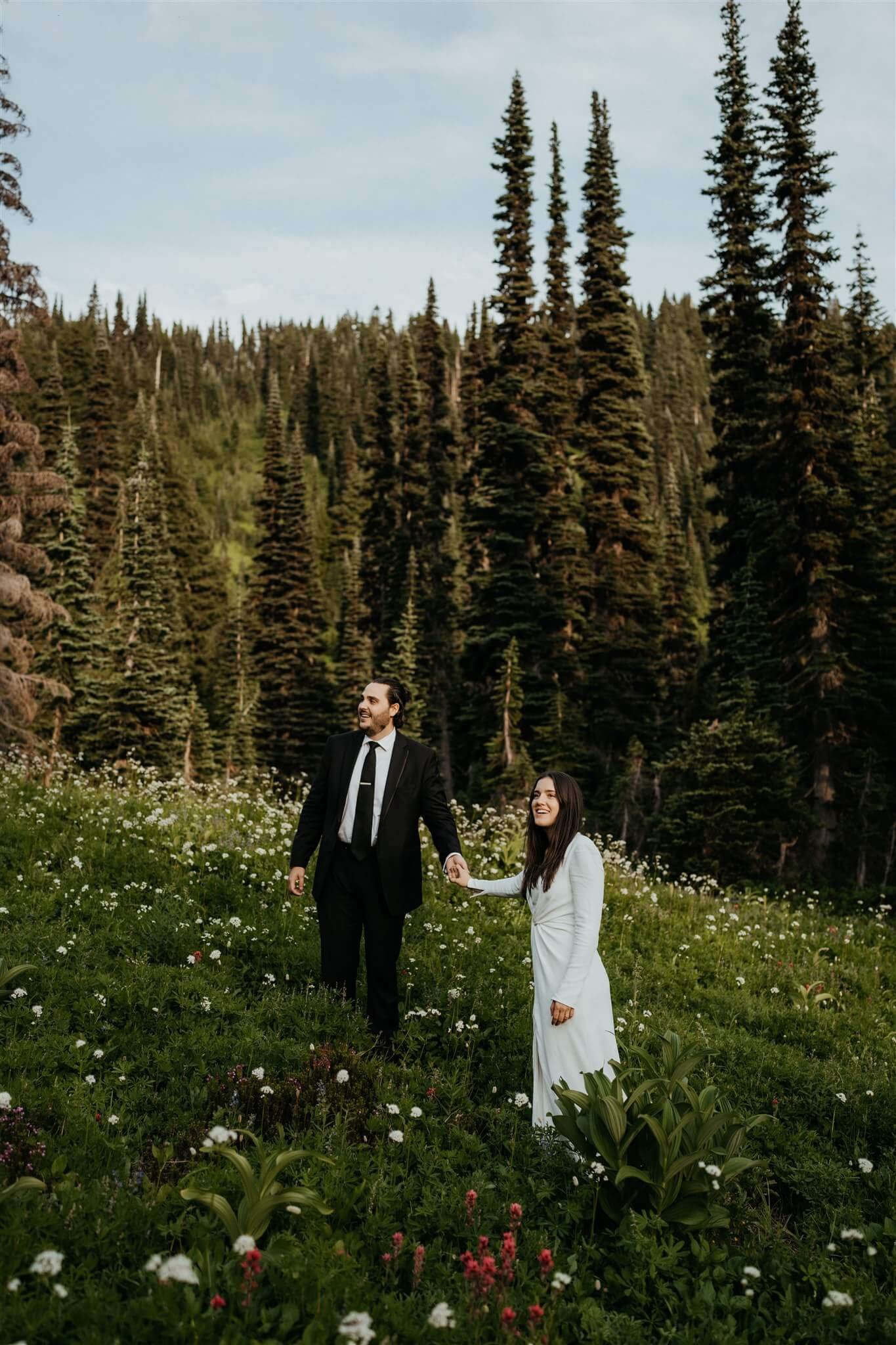 Bride and groom hold hands while standing in a wildflower field at Mount Rainier adventure wedding