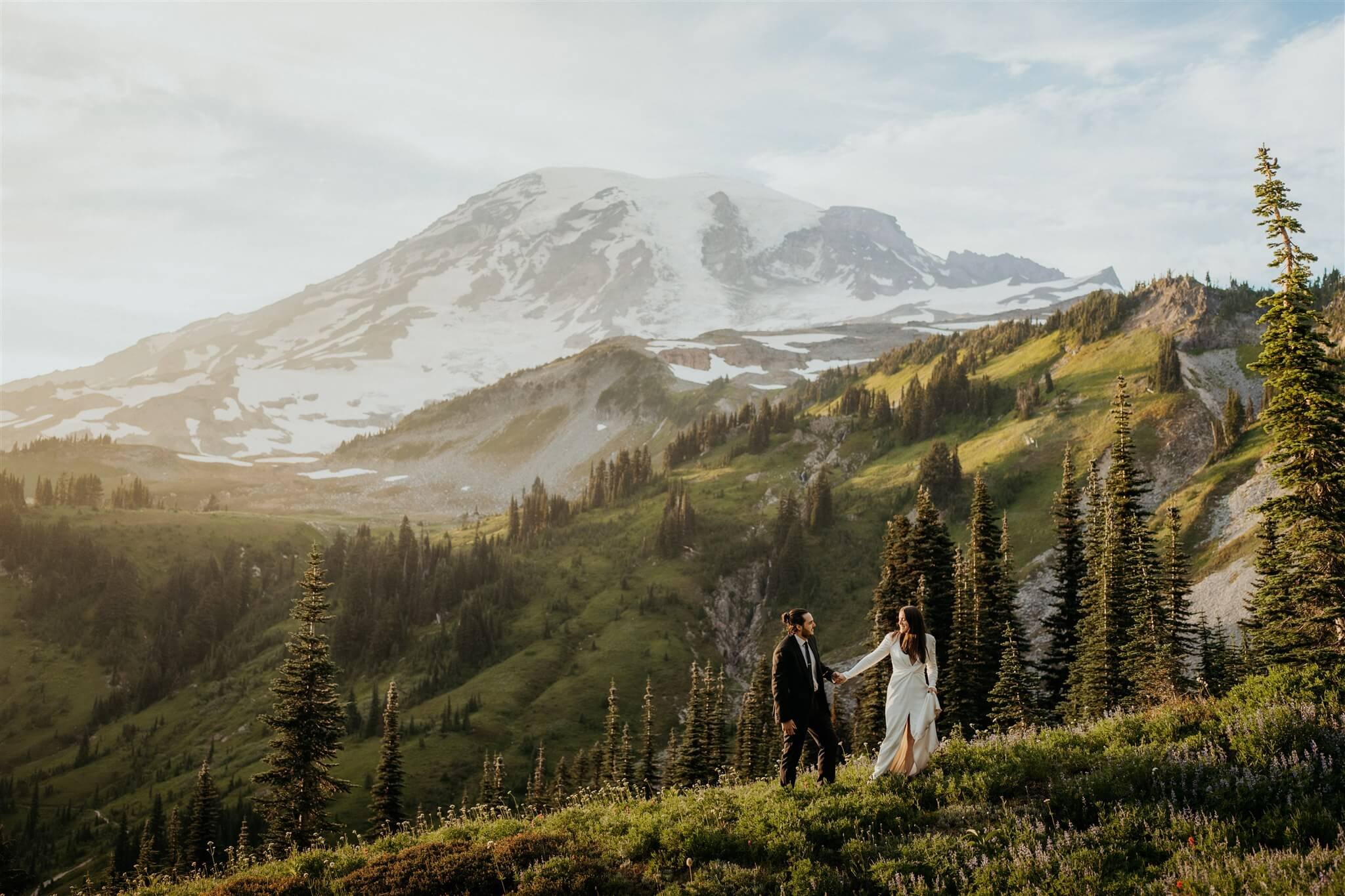 Bride and groom hold hands while walking along a trail at Mt Rainier adventure wedding