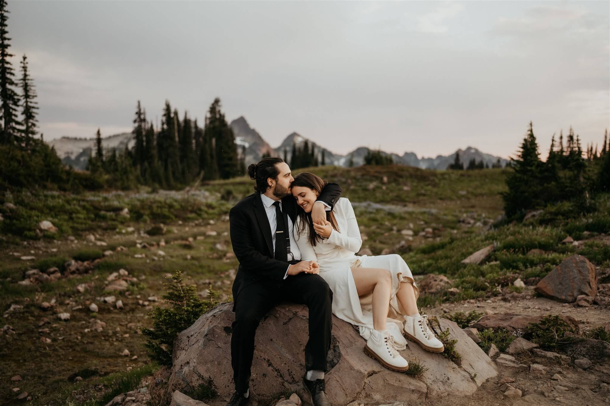 Bride and groom sitting on a rock, cuddling during sunset elopement photos at Mt Rainier