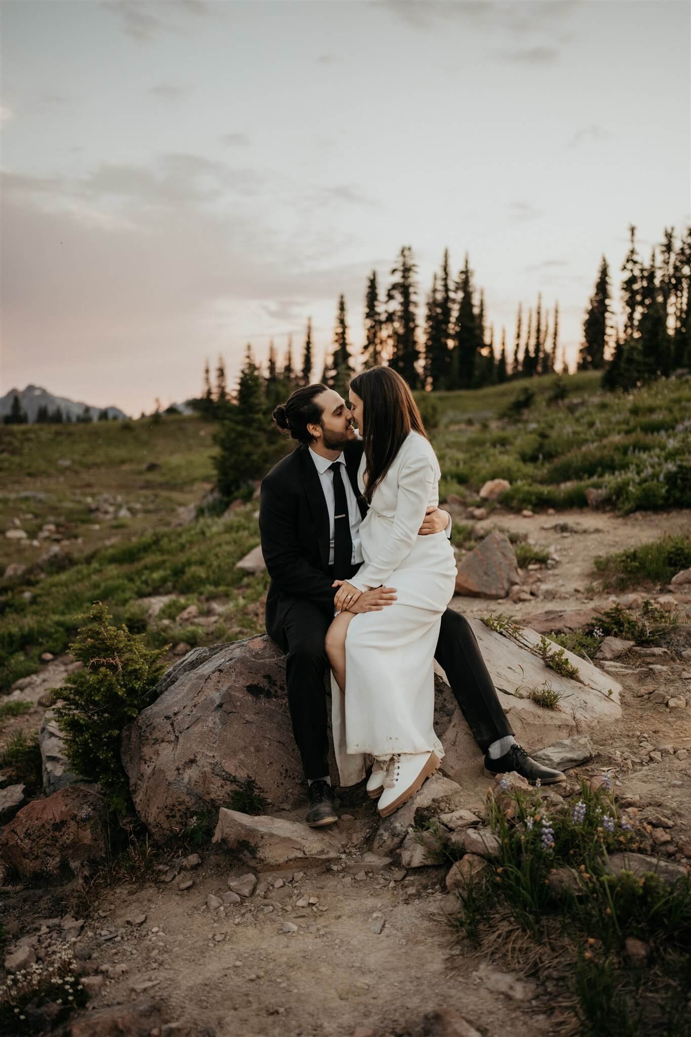 Bride and groom sitting on a rock, kissing during sunset elopement photos at Mt Rainier adventure wedding