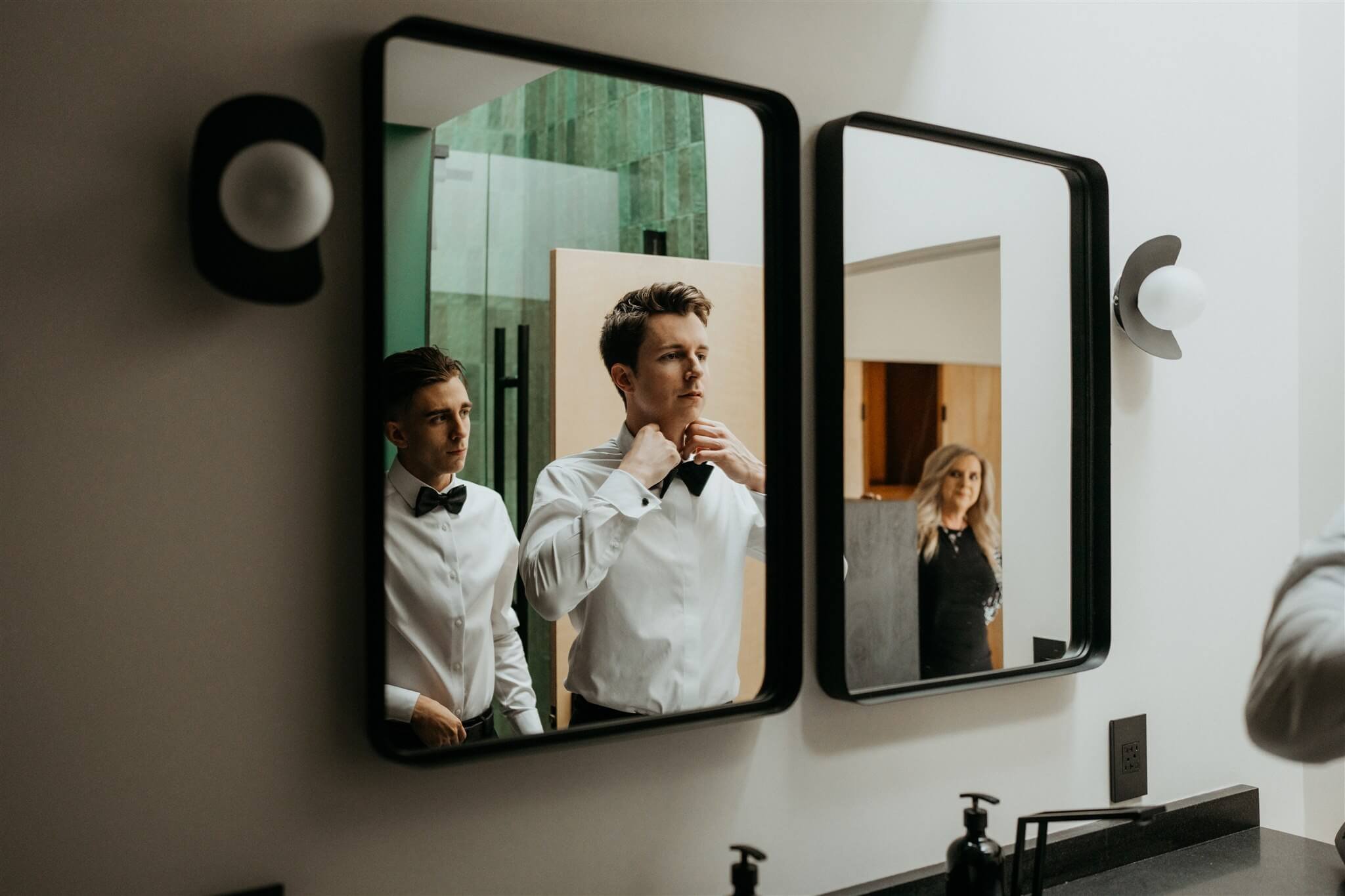 Groom adjusting bow tie in the bathroom mirror before elopement in the North Cascades