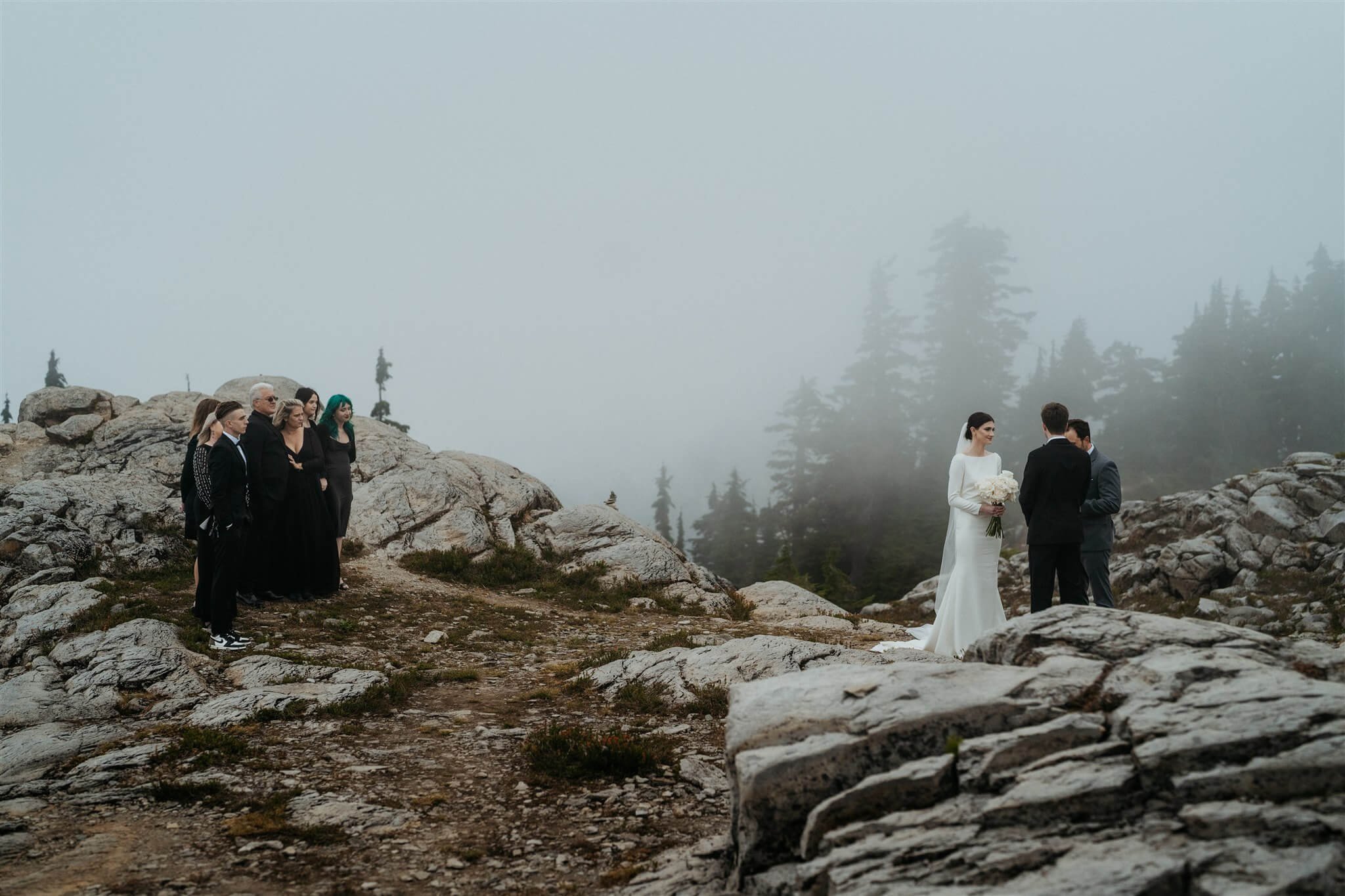 Bride and groom exchanging vows in the mountains at foggy Artist Point elopement while friends and family watch from a distance