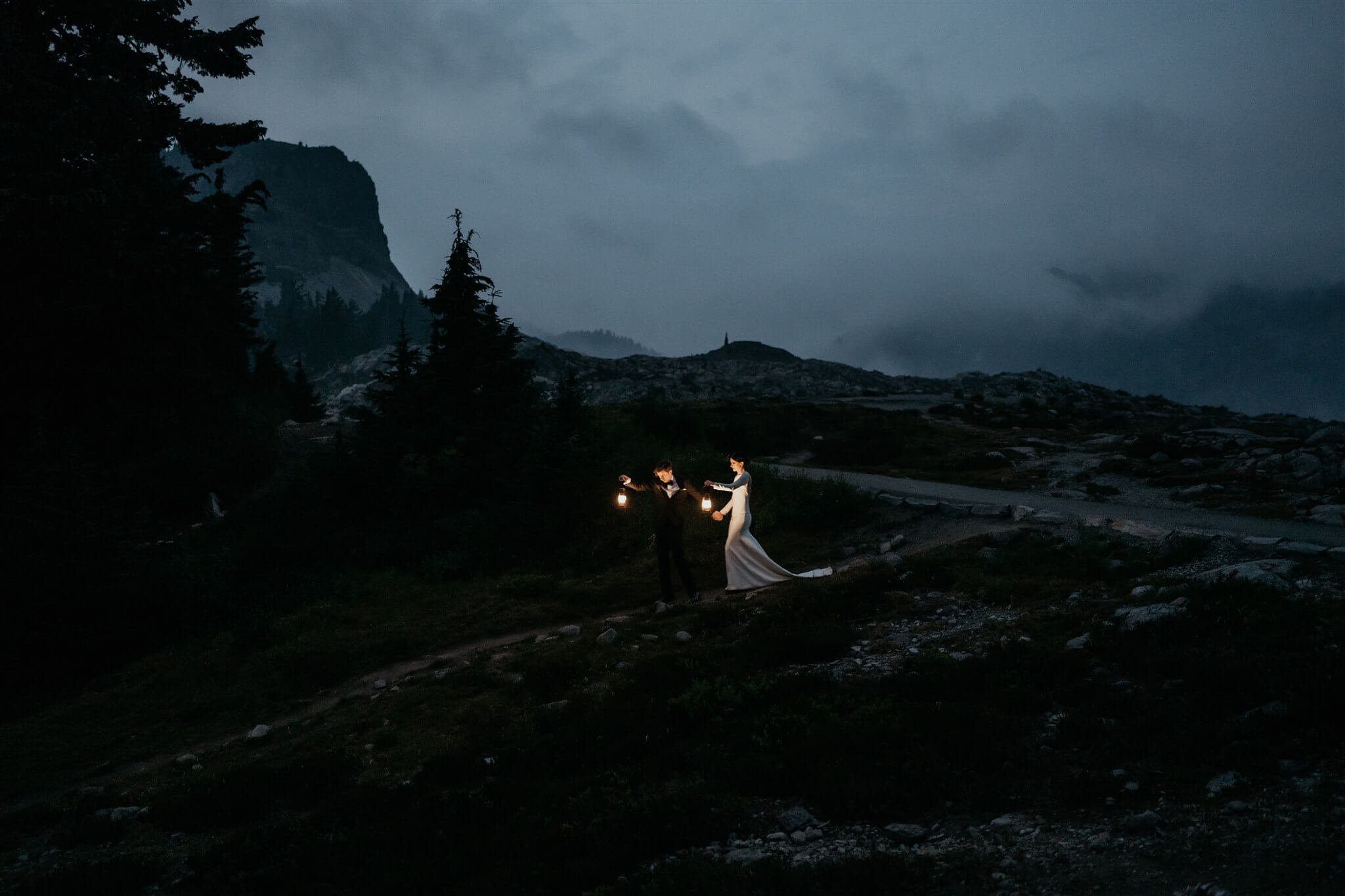 Bride and groom holding lanterns, walking through the dart at the end of their foggy Artist Point elopement