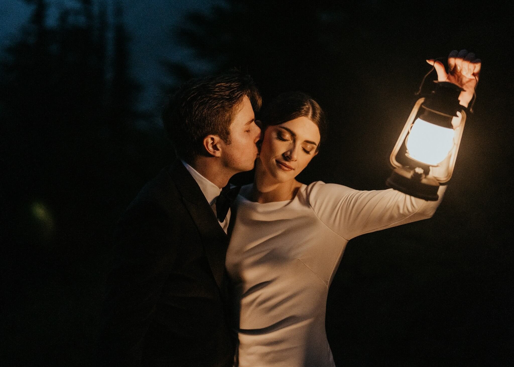 Groom kissing bride while holding lanterns, during their foggy Artist Point elopement