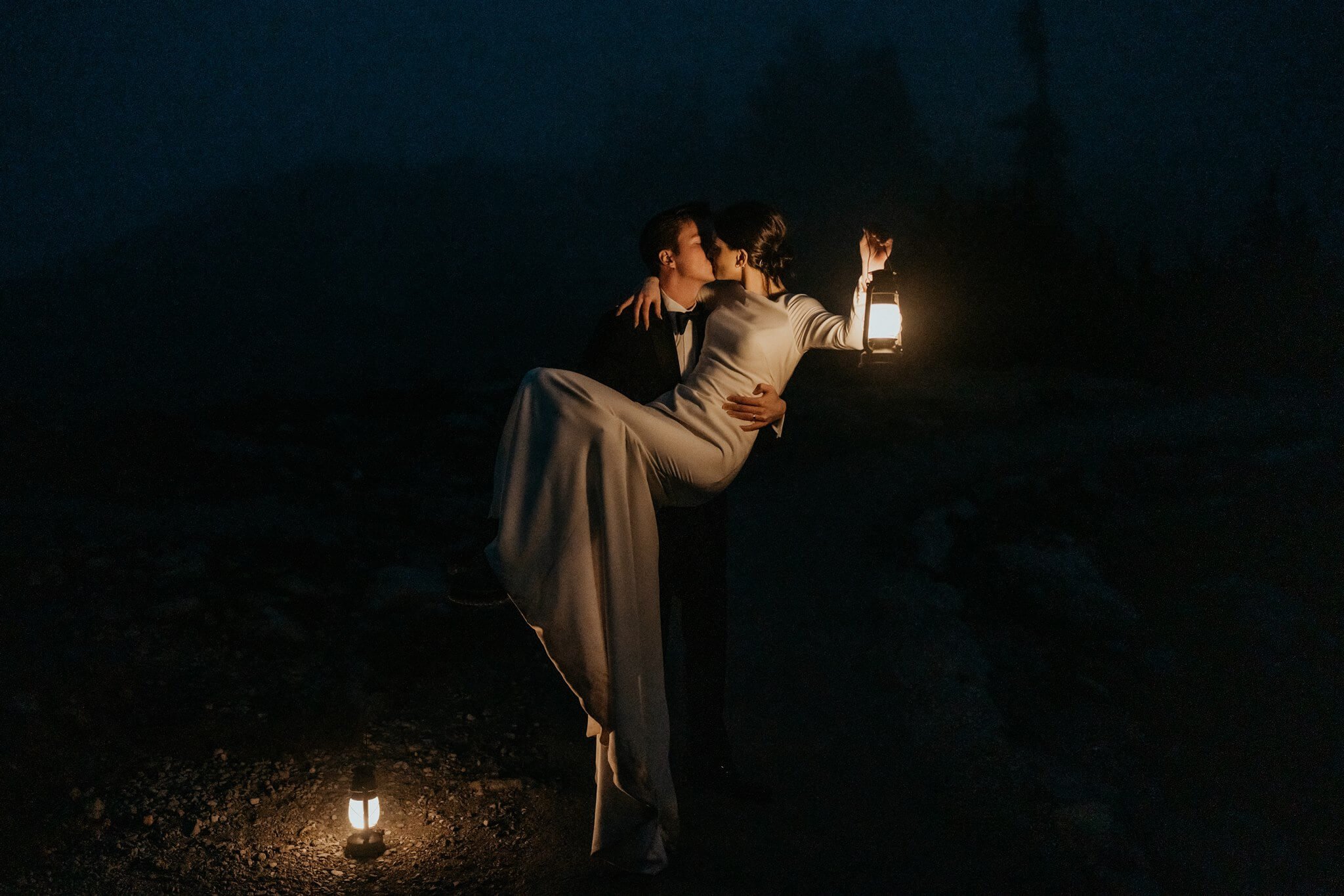 Groom carrying bride while holding lanterns in the dark