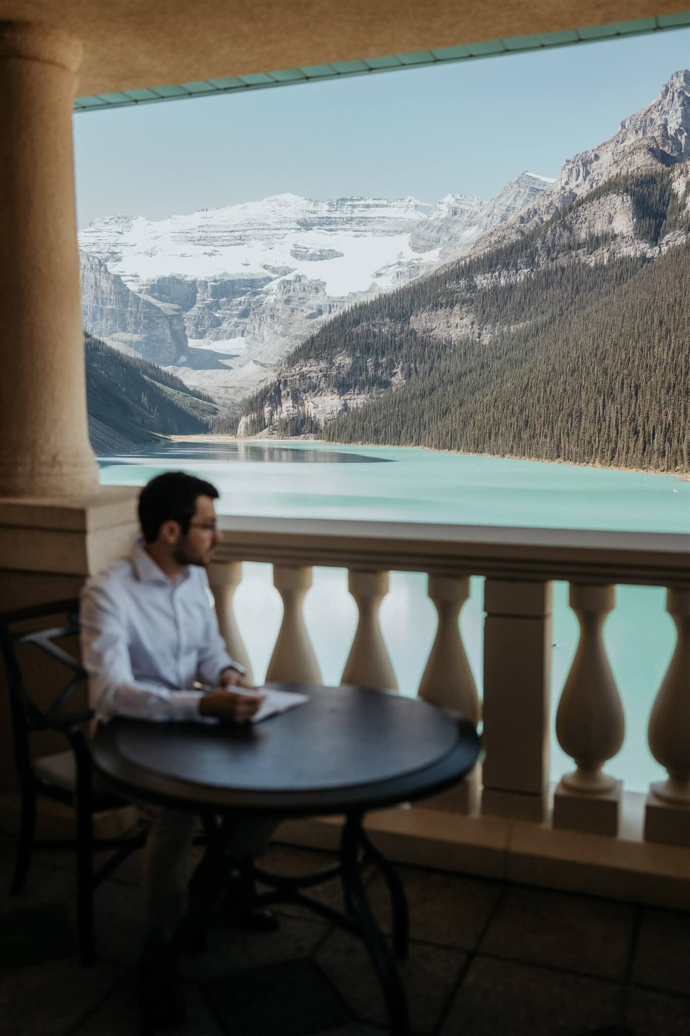Groom sitting at a table on the patio at Fairmont Chateau Lake Louise writing handwritten vows
