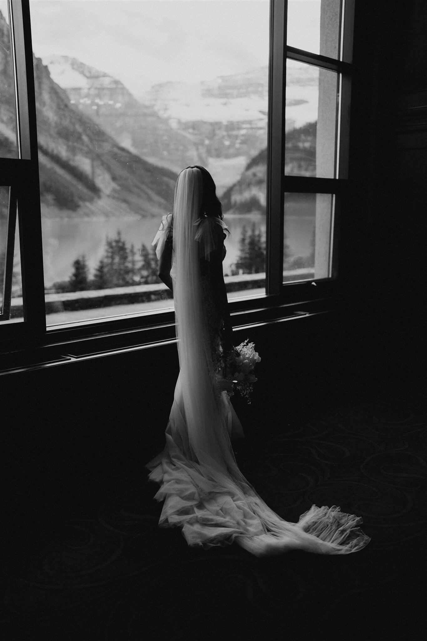 Bride standing in Fairmont Chateau hotel looking out the window at Lake Louise