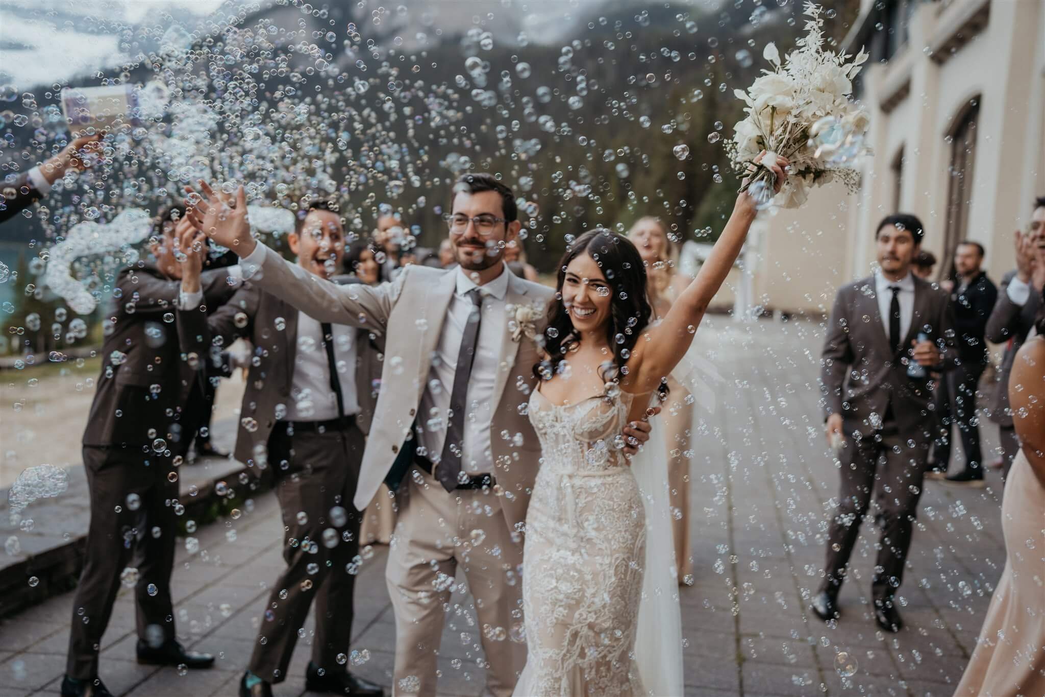 Bride and groom cheer while guests blow bubbles at Lake Louise wedding in Alberta Canada