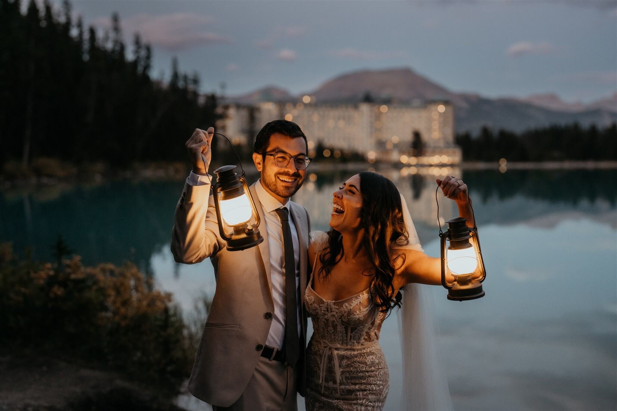 Bride and groom holding lanterns by Lake Louise at their luxury wedding at Fairmont Chateau Lake Louise hotel