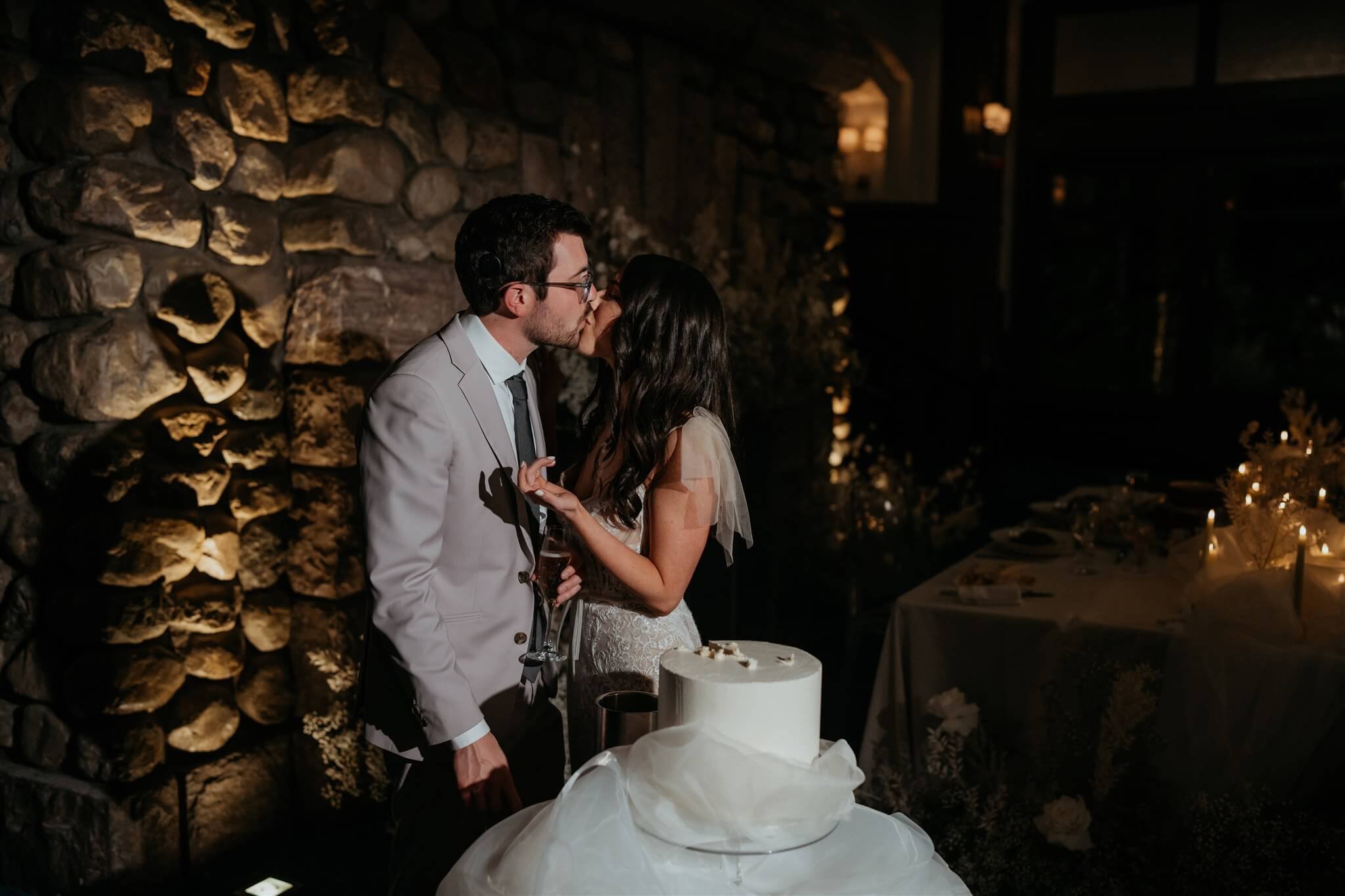 Bride and groom kiss after cutting white wedding cake at Lake Louise wedding 