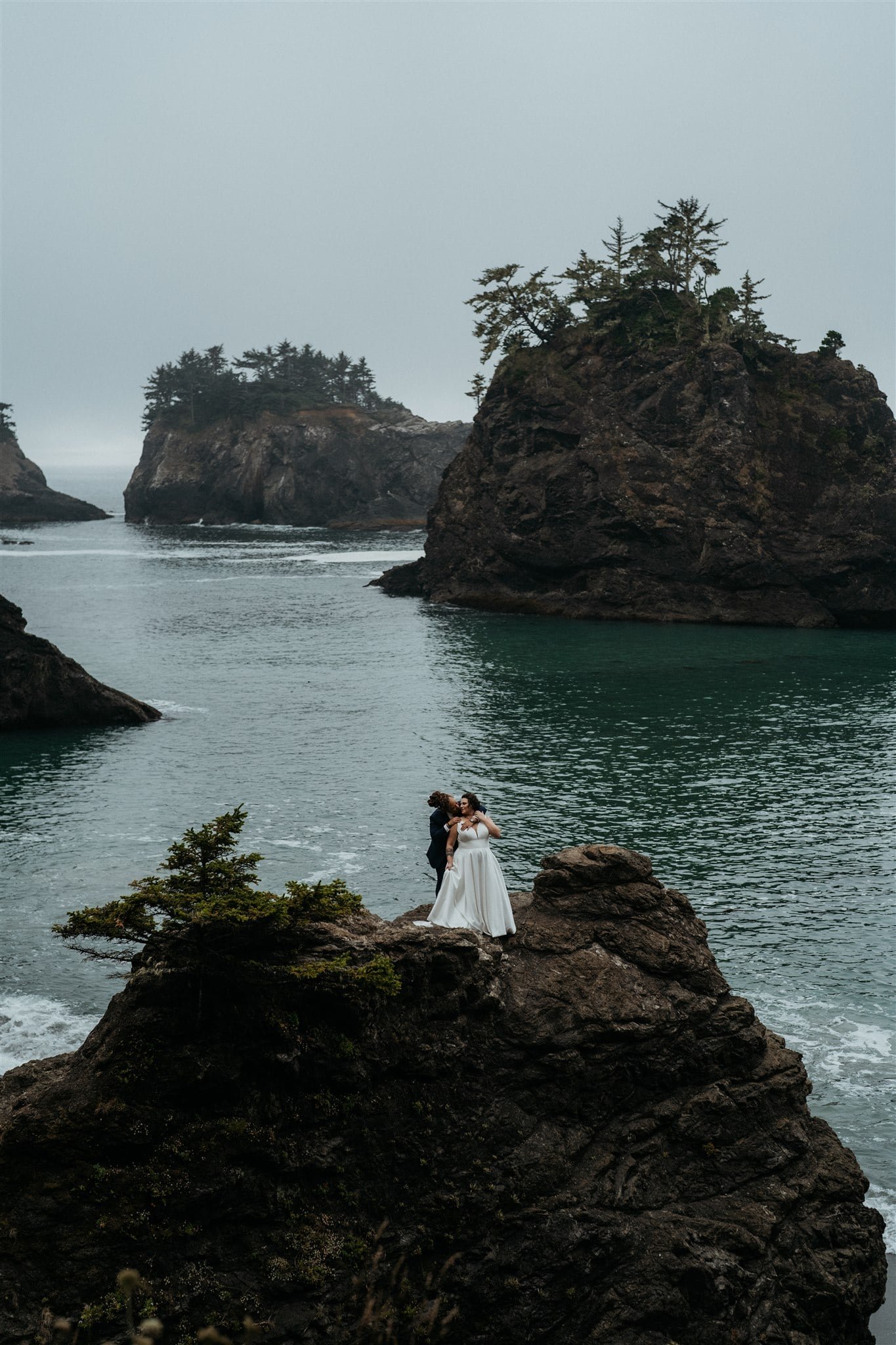 Brides stand on the rocky coast on the beach of their Oregon Coast elopement