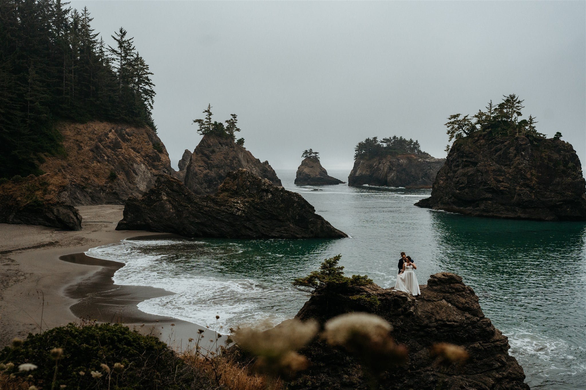 Brides stand on the rocky coast on the beach during their Oregon Coast elopement