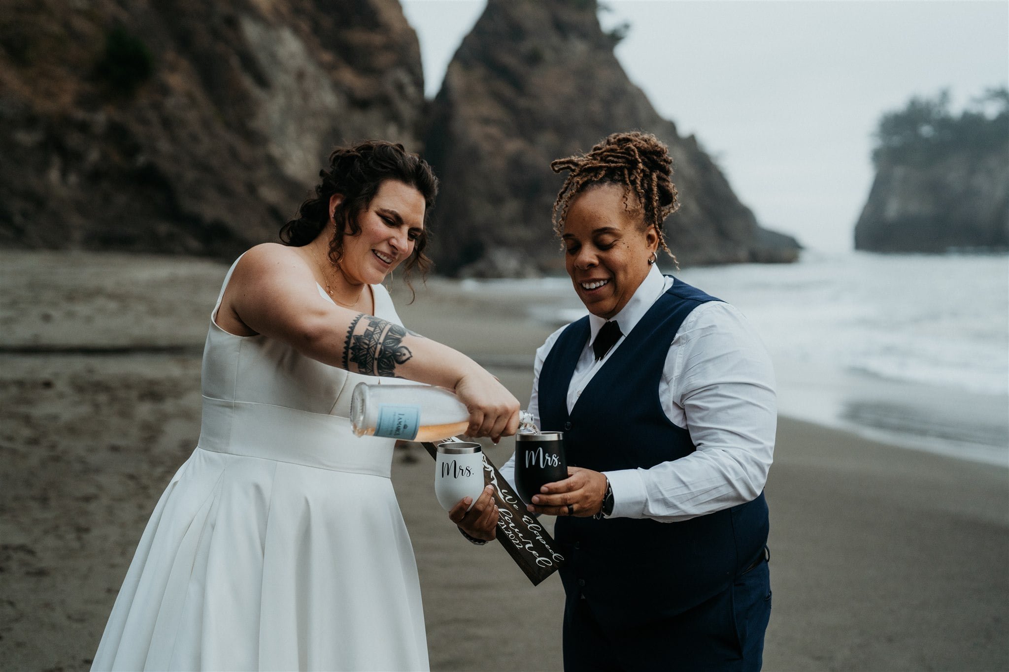 Brides pour champagne into custom mugs during their Southern Oregon Coast elopement on the beach