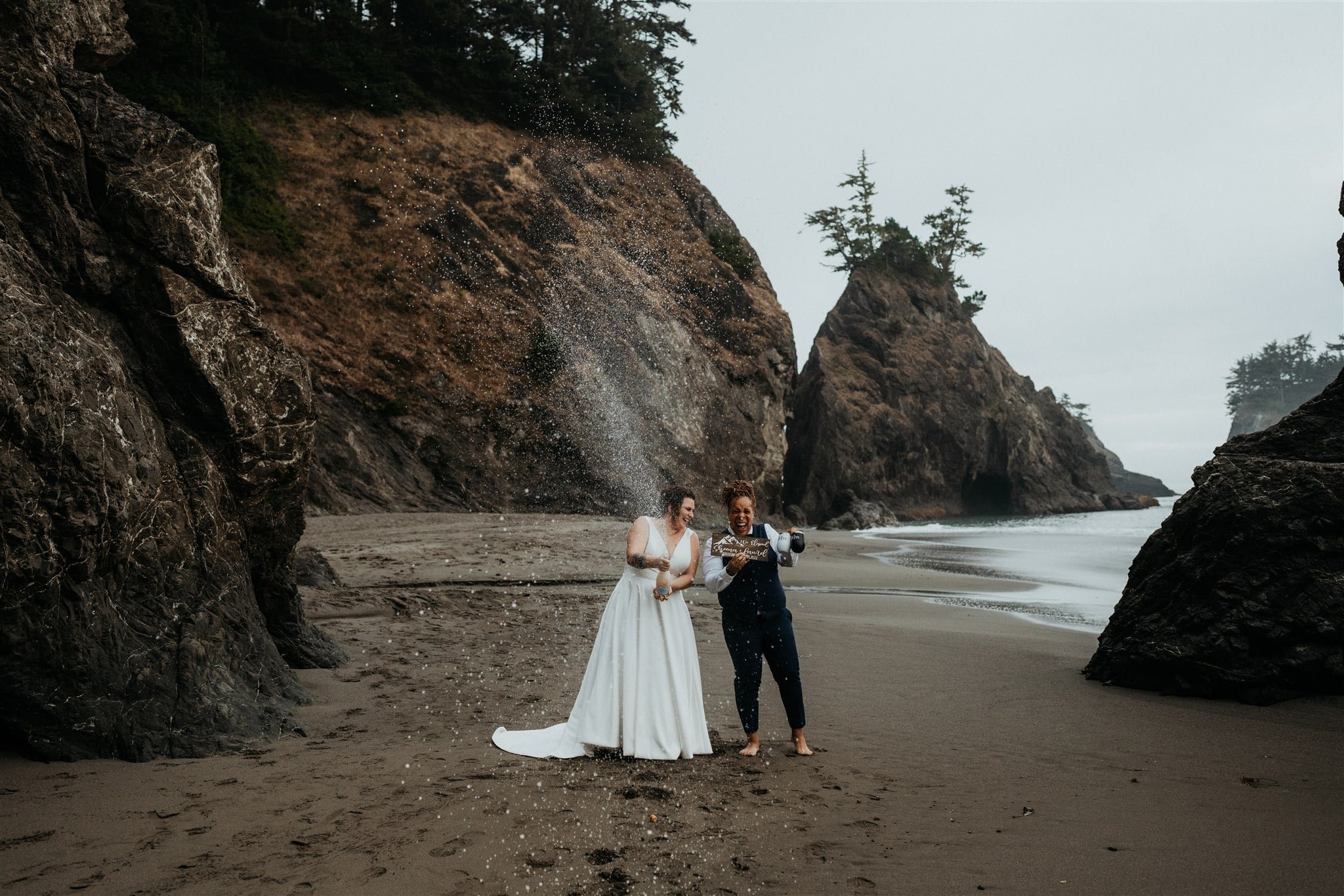 Brides spray champagne on the beach during their Southern Oregon Coast elopement