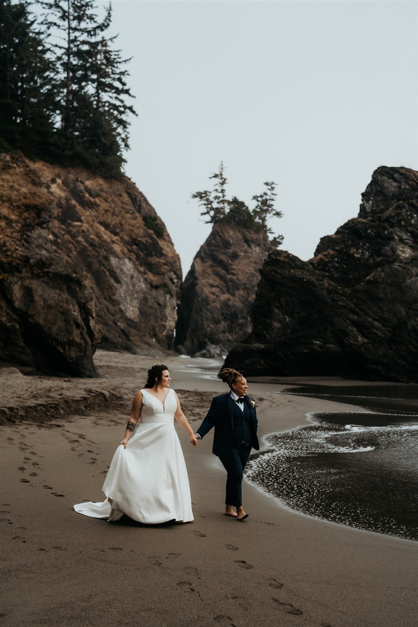 Brides holding hands while strolling along the beach on the Oregon Coast