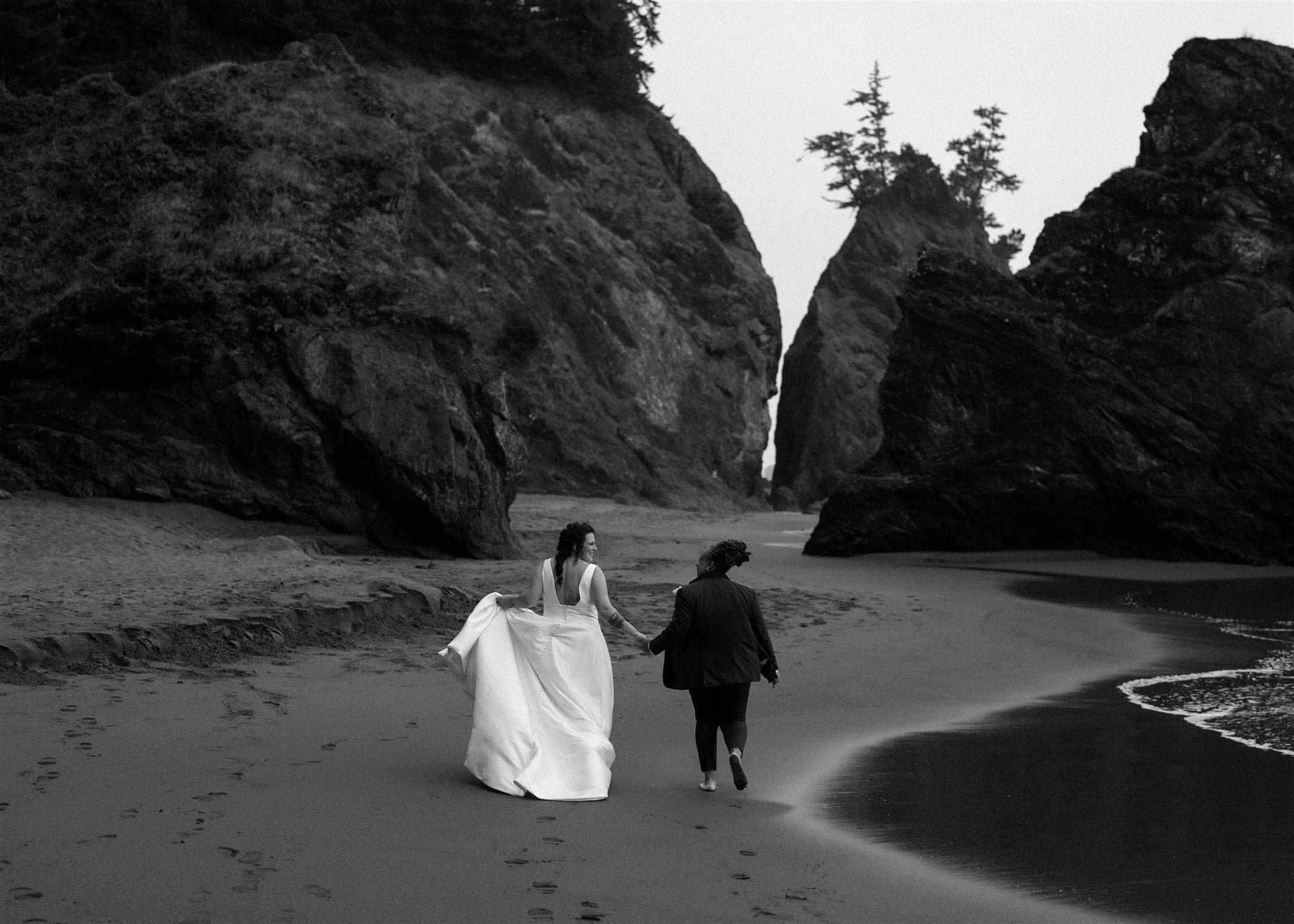 Brides holding hands while strolling along the beach on the Oregon Coast