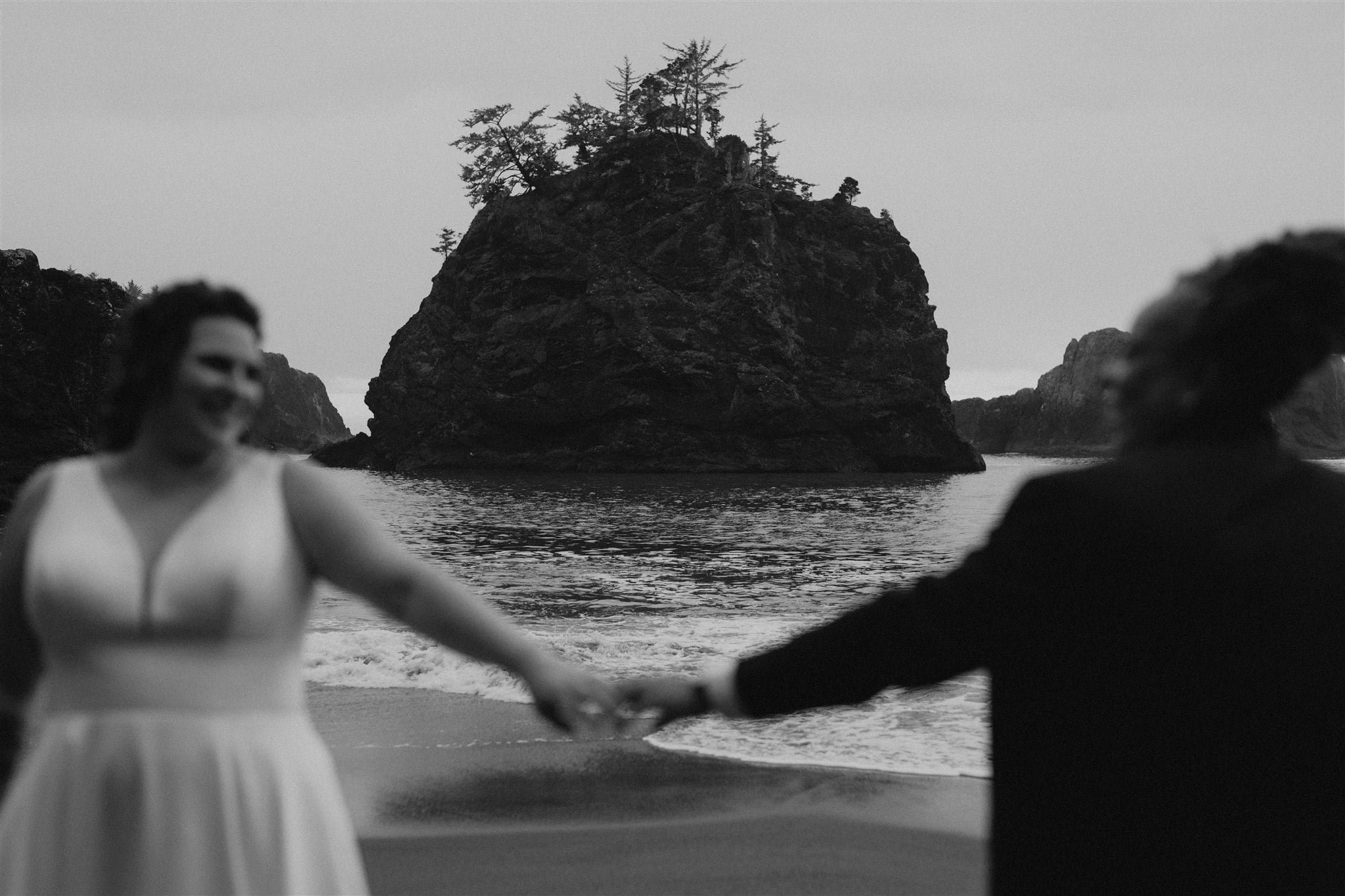 Two brides hold hands on the beach during their Oregon Coast elopement