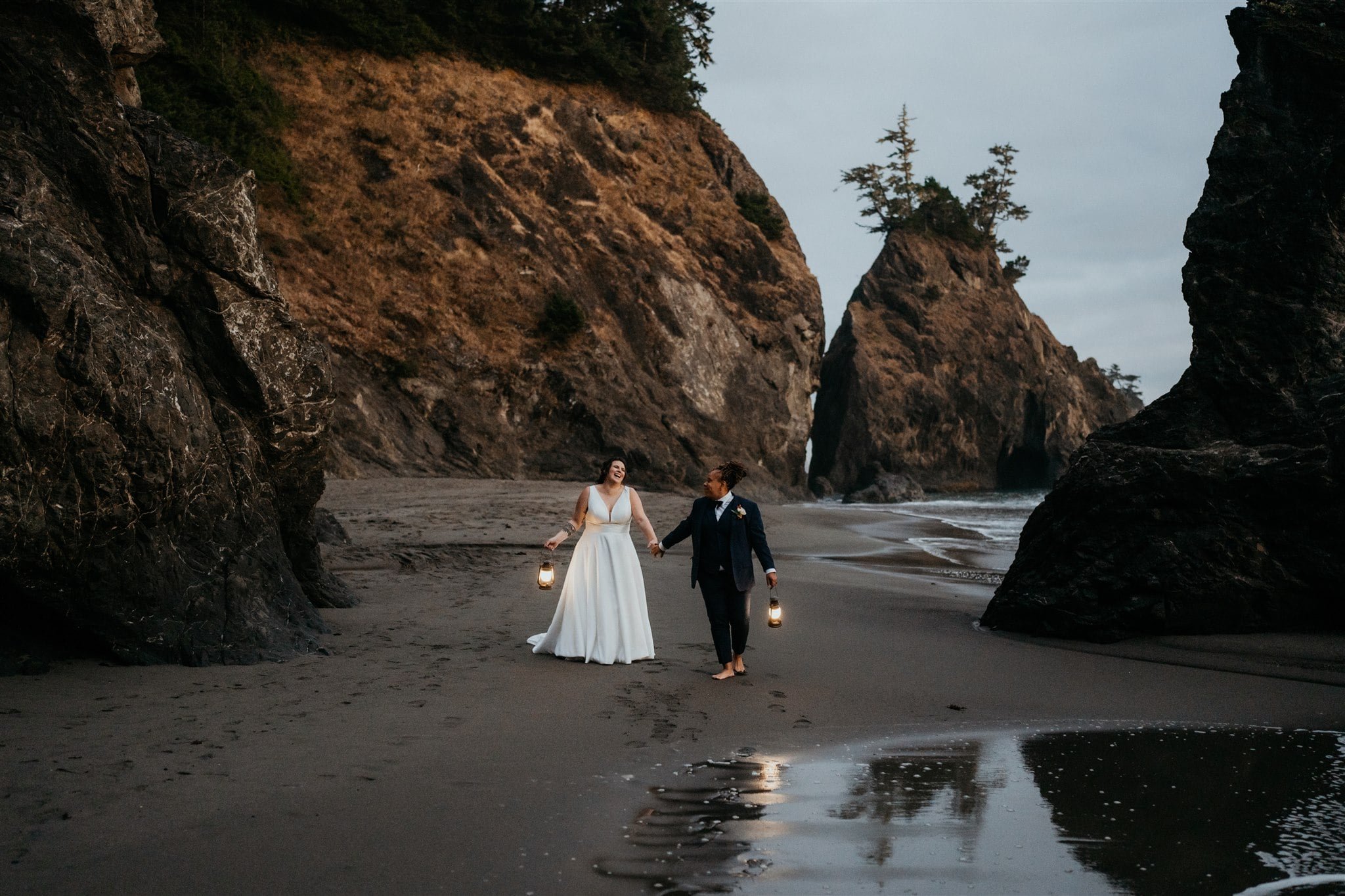 Two brides holding hands and walking along the beach during their blue hour elopement portraits