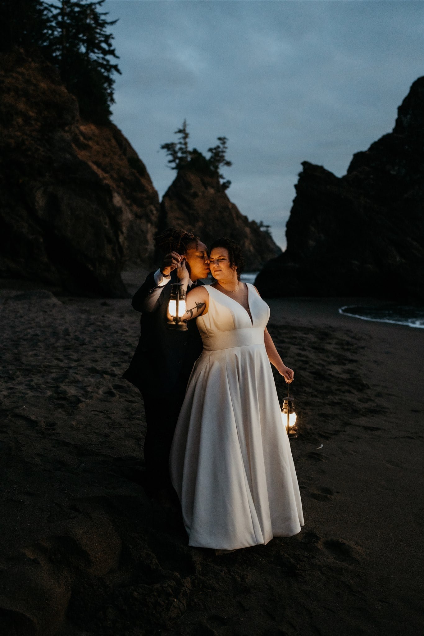 Two brides kissing and holding lanterns on the beach during their Southern Oregon Coast elopement
