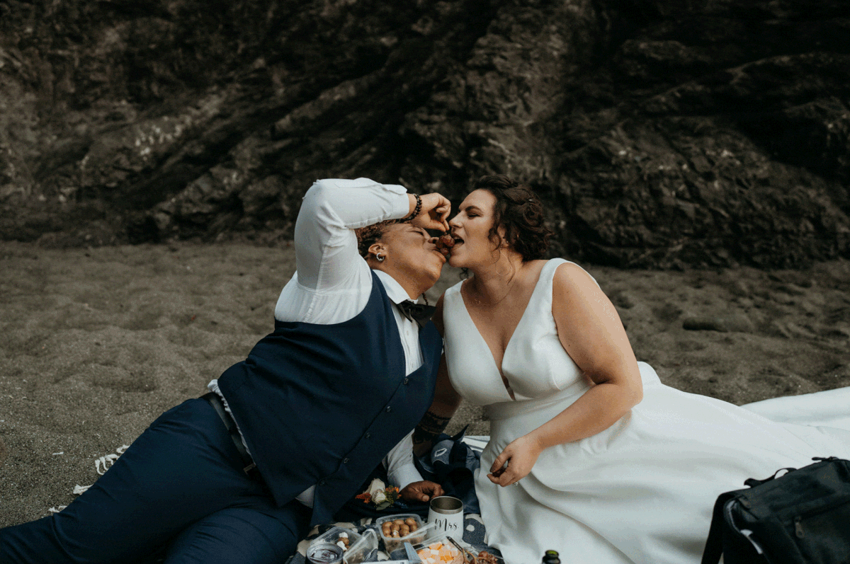 Two brides share fruit during their beach picnic on the Southern Oregon Coast