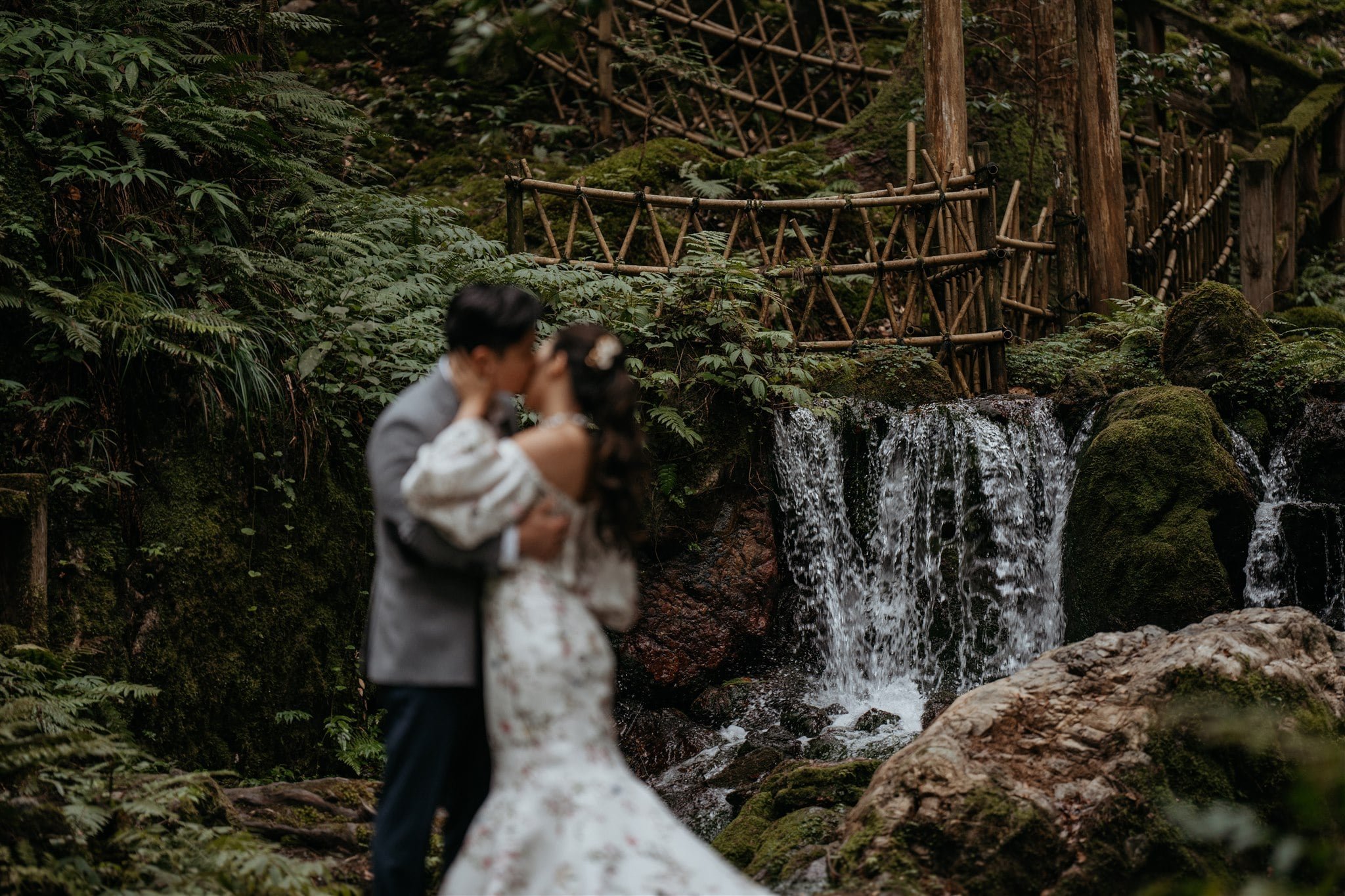 Bride and groom kiss in front of a waterfall in the forest for their Japan elopement portraits