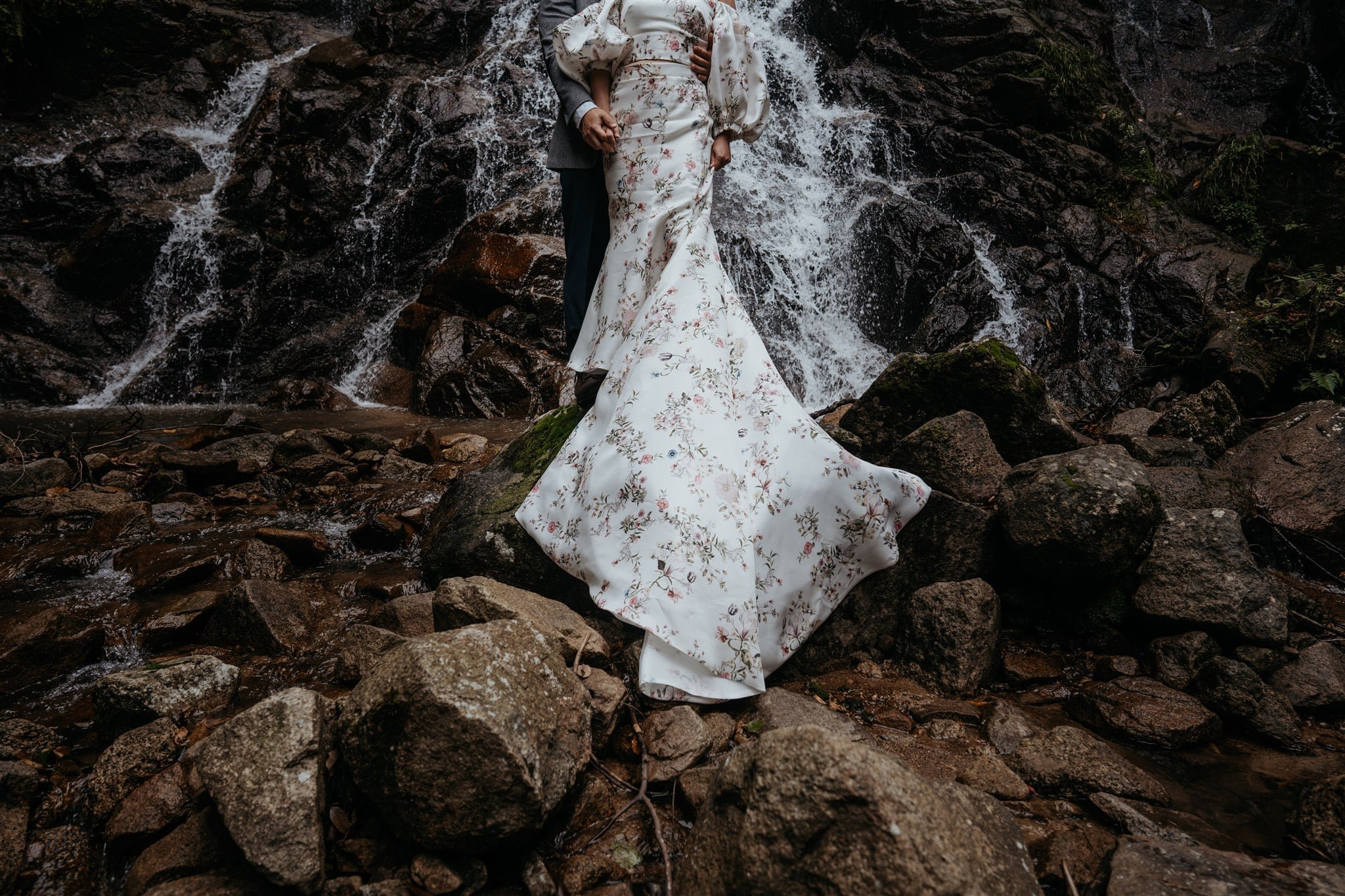 Bride and groom standing on rocks in front of a waterfall in the forest for their Japan elopement portraits