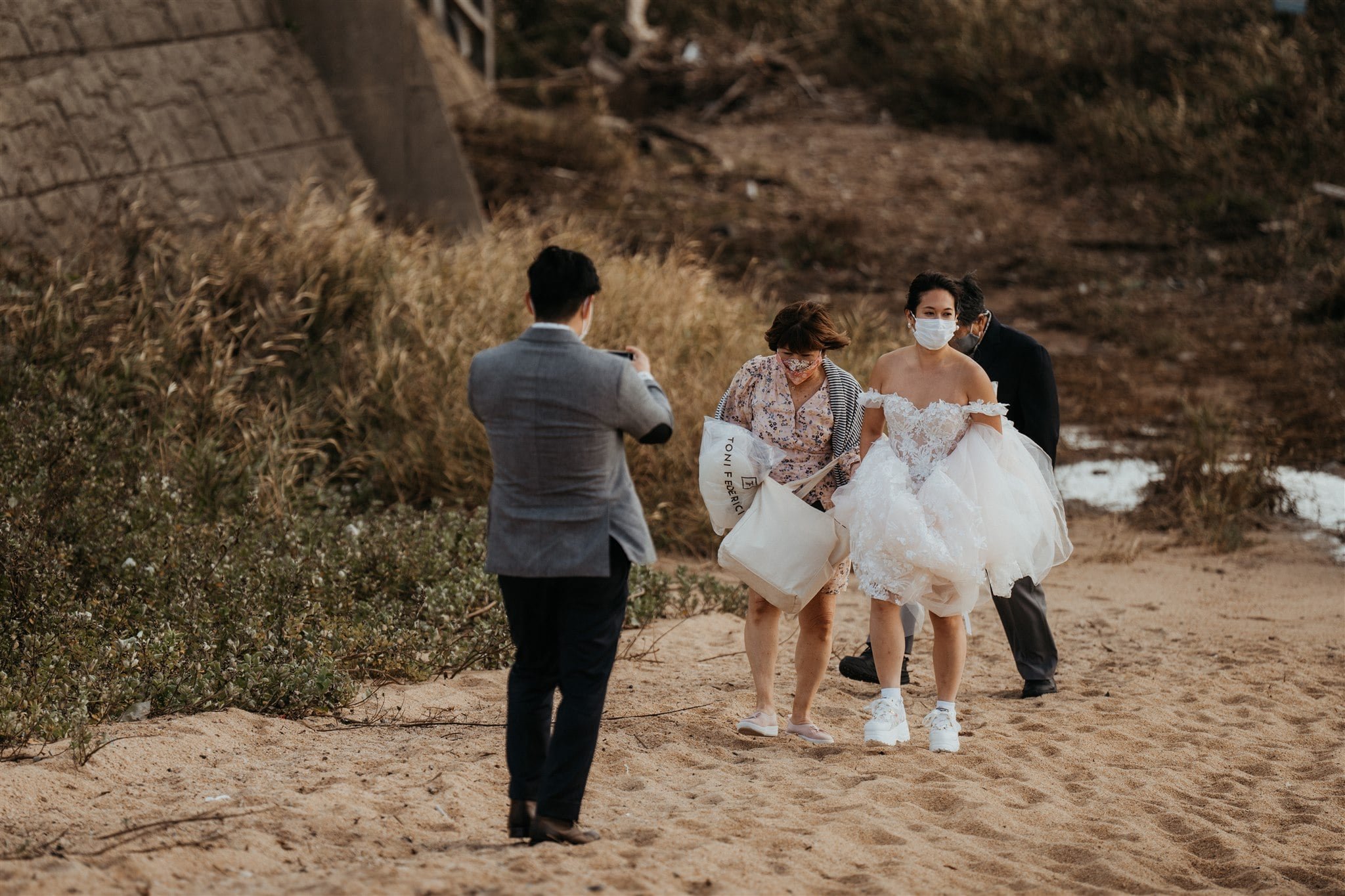 Groom taking photos of the bride and her parents walking across the beach for their outdoor elopement ceremony