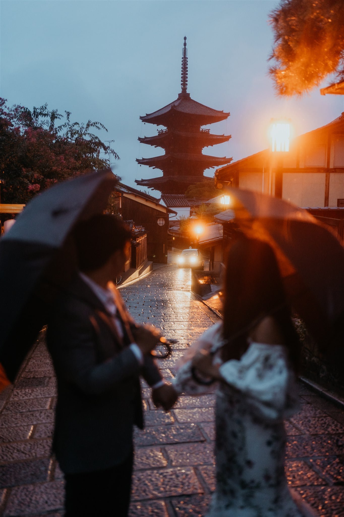 Bride and groom holding hands while walking with umbrellas during blue hour after their elopement in Japan