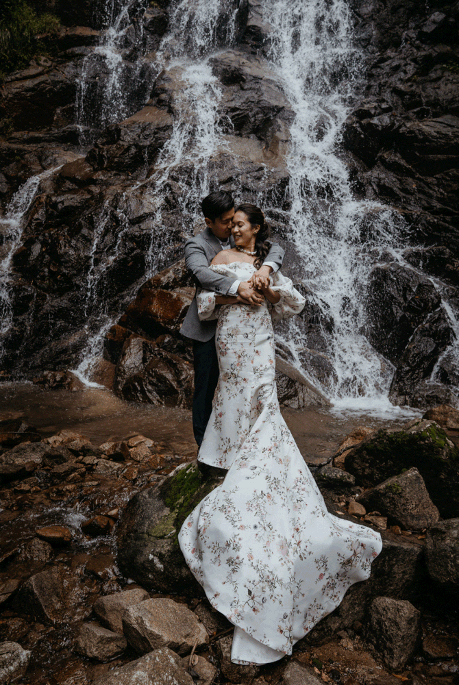 Bride and groom standing on rocks in front of a waterfall in the forest for their Japan elopement portraits