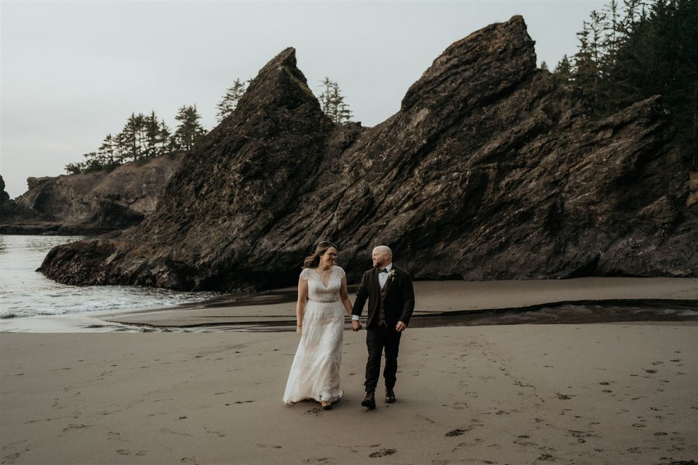 Bride and groom holding hands while walking across the beach during their Oregon Coast elopement