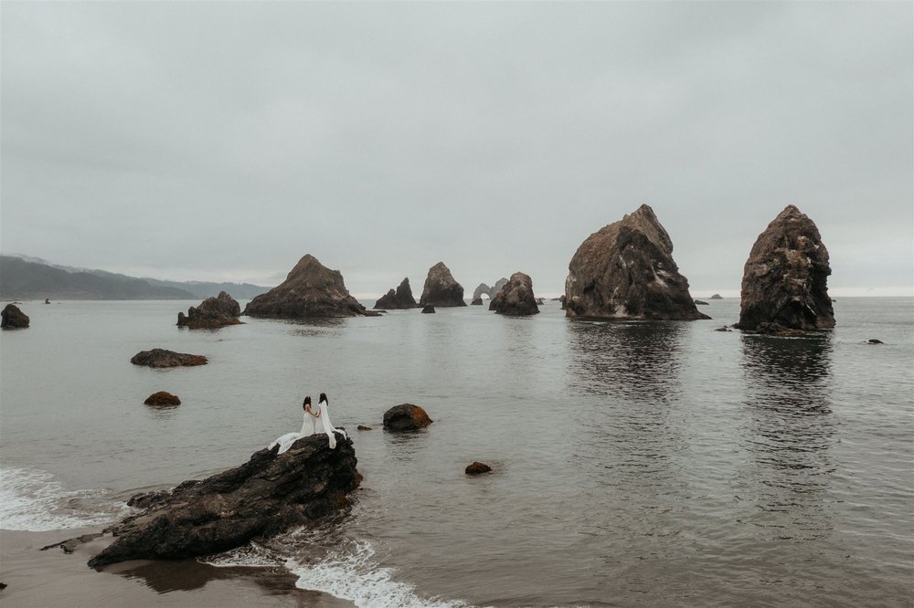 Two brides standing on a rocky beach during their Southern Oregon Coast elopement