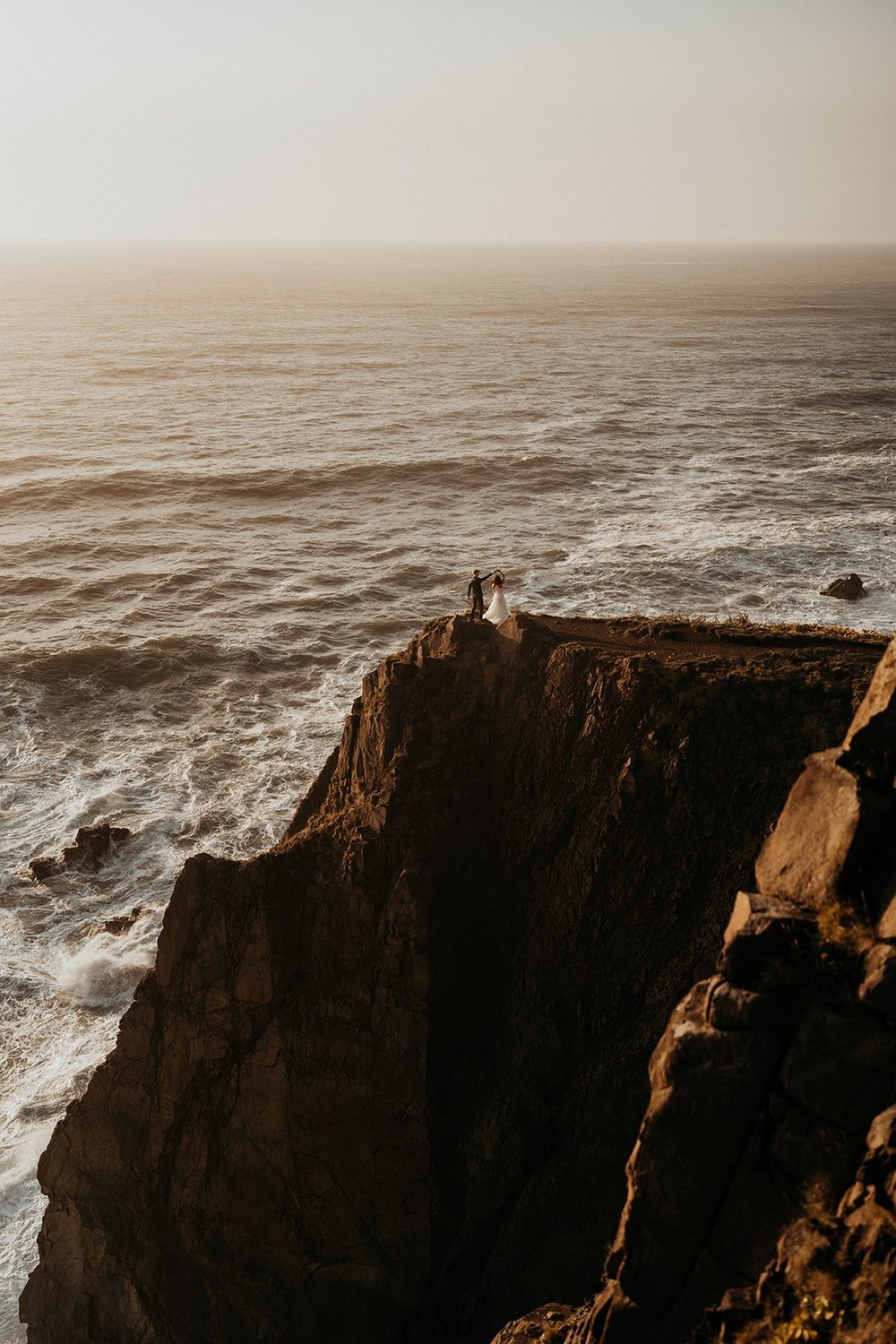Two brides standing on a cliff during their Oregon Coast elopement