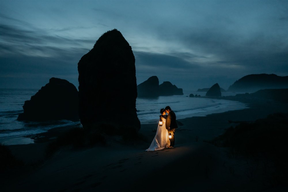 Brides holding lanterns on the beach during their Oregon Coast elopement