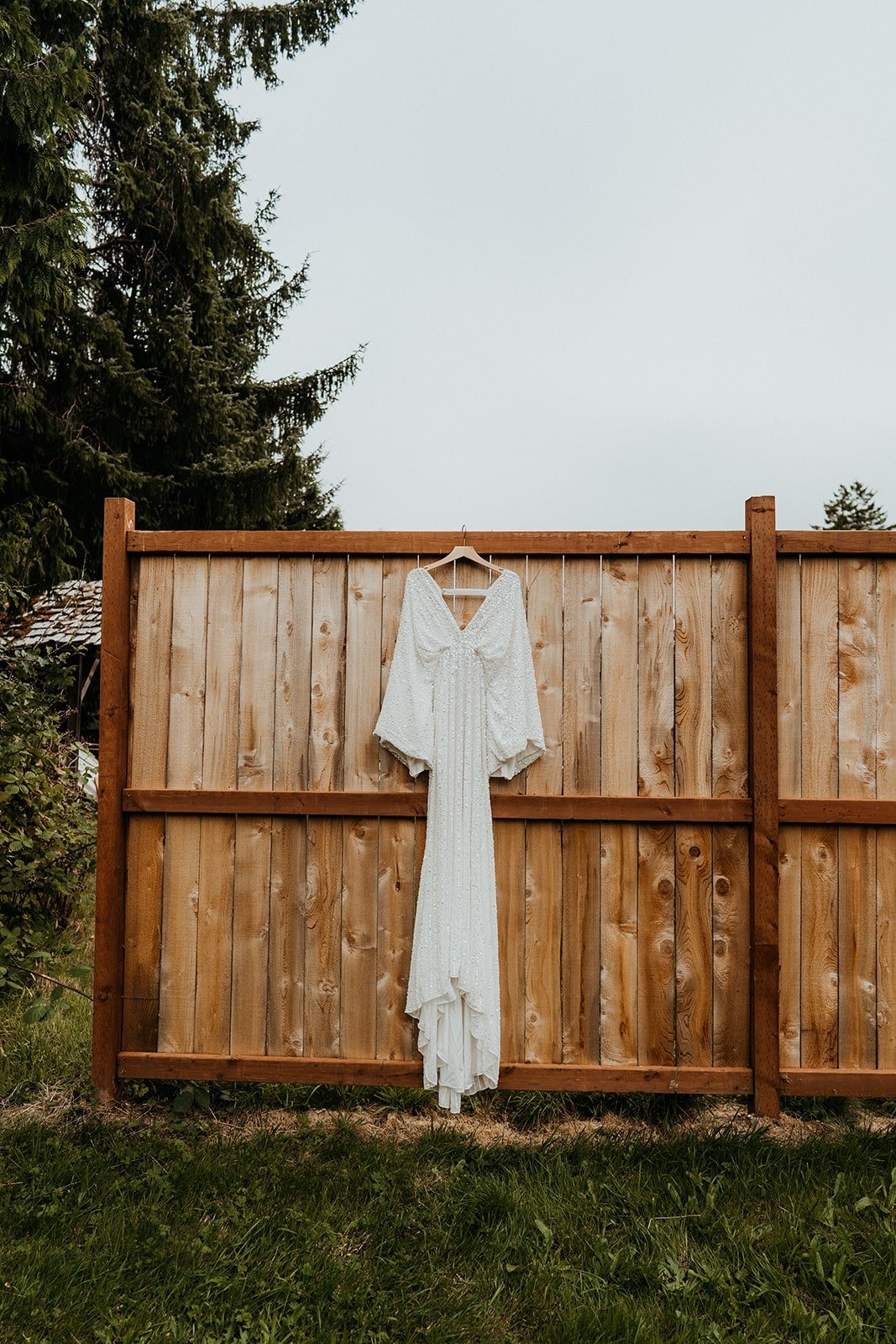 White boho wedding dress hanging on wood fence